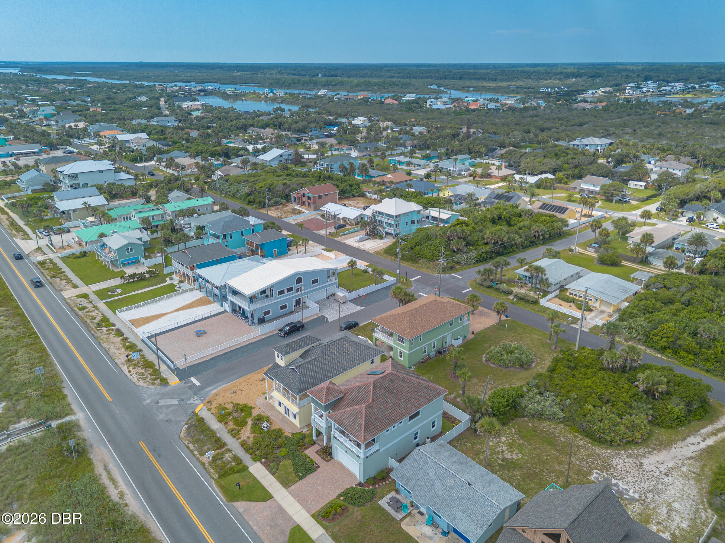 Aerial view of coastal homes along a two-lane road, with wetlands and waterways in the distance.