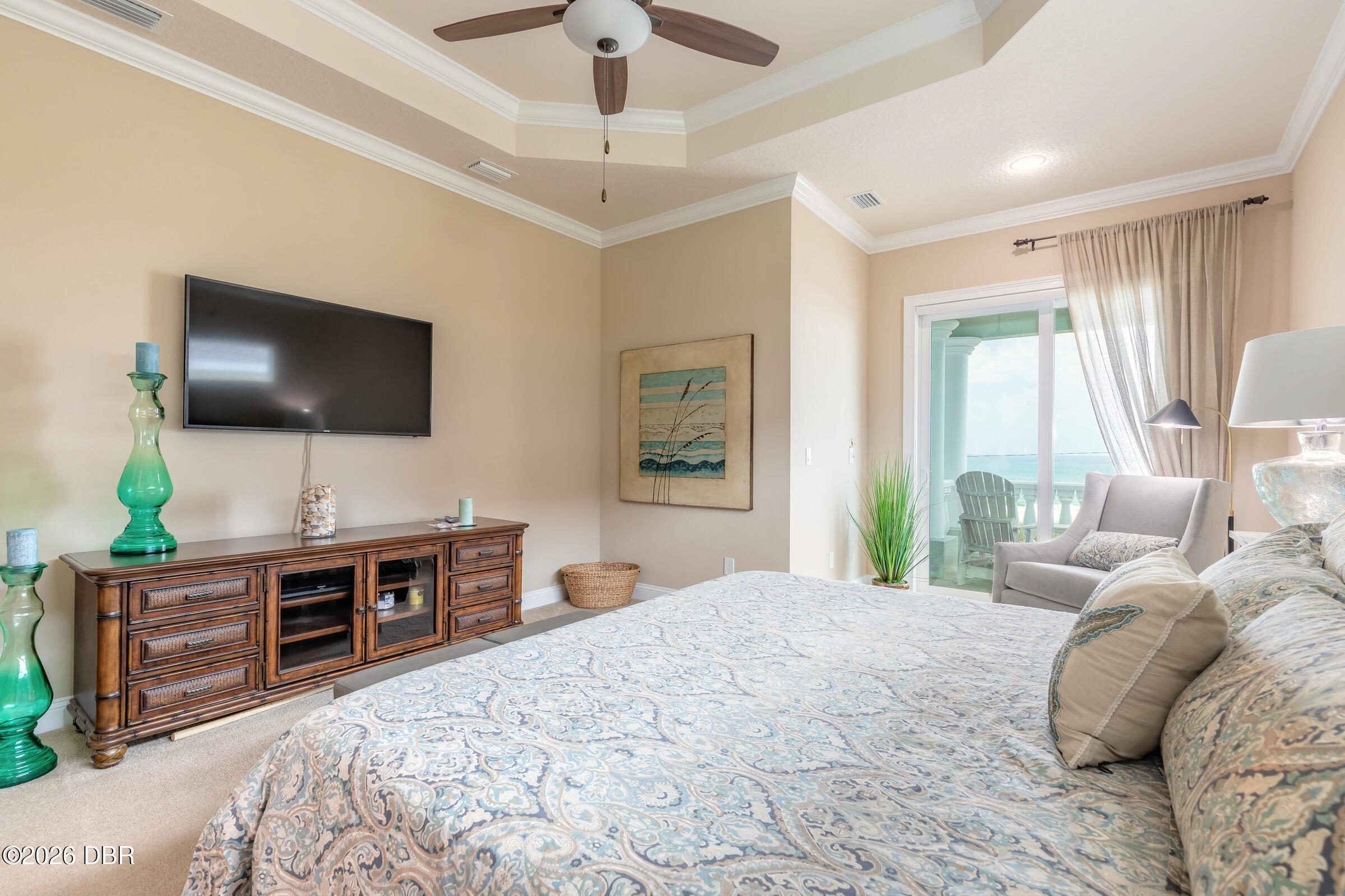 Bedroom with patterned bedding, a wall-mounted TV, and ocean views through the balcony door.