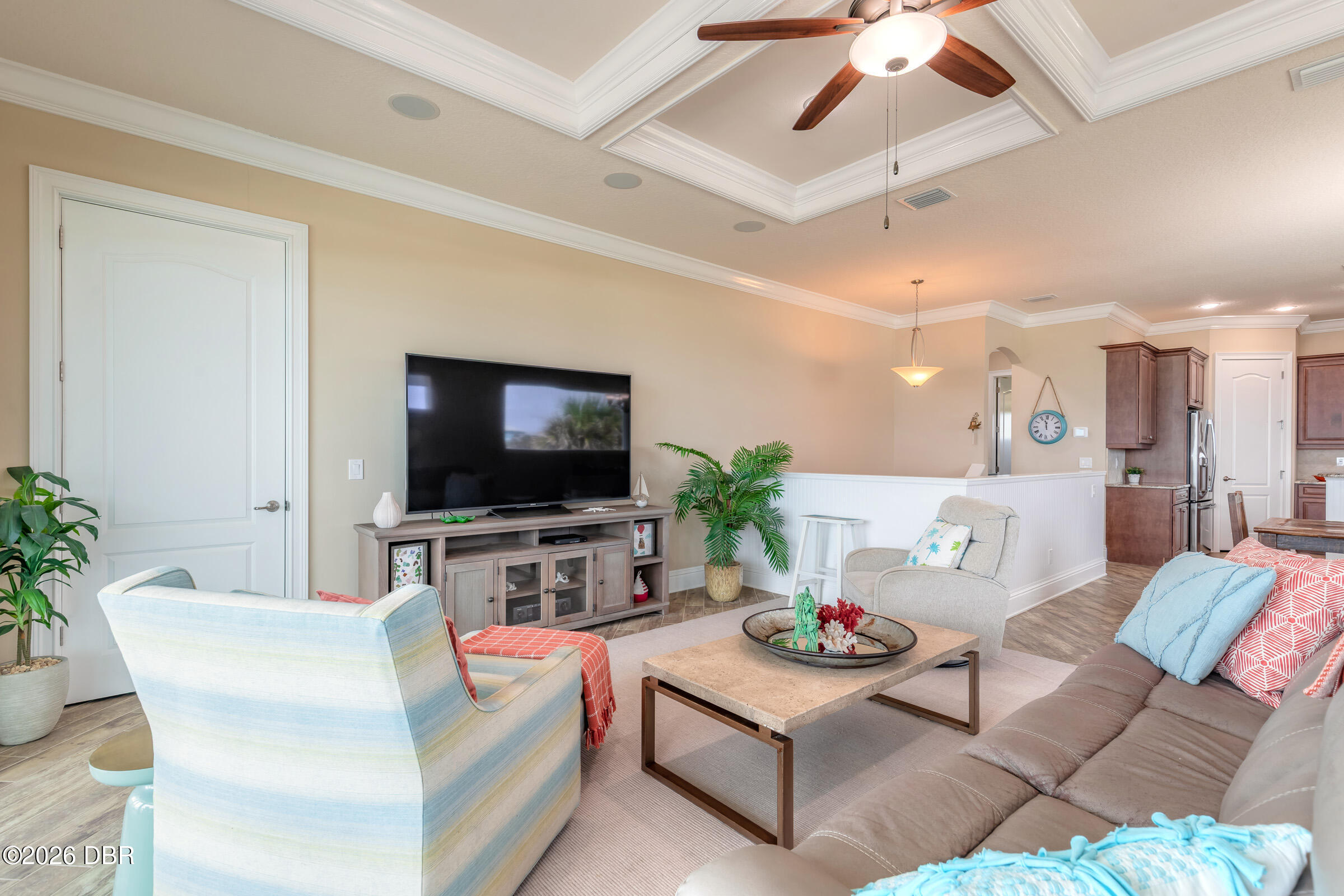 Furnished living room with a tray ceiling, ceiling fan, TV, and open kitchen.