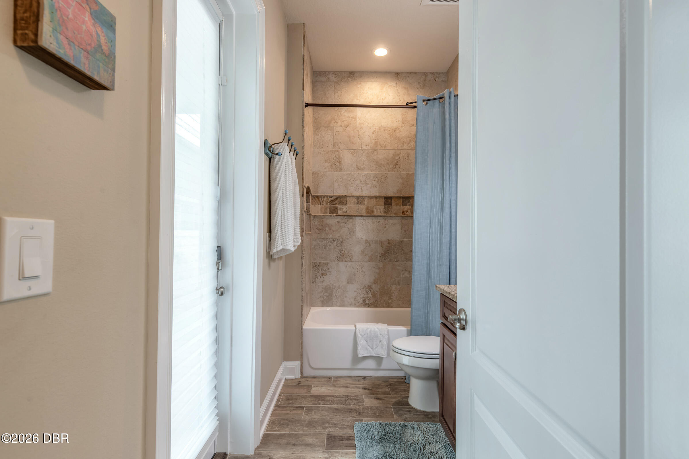 Bathroom with a tiled tub and shower, blue curtain, white toilet, and dark wood vanity.