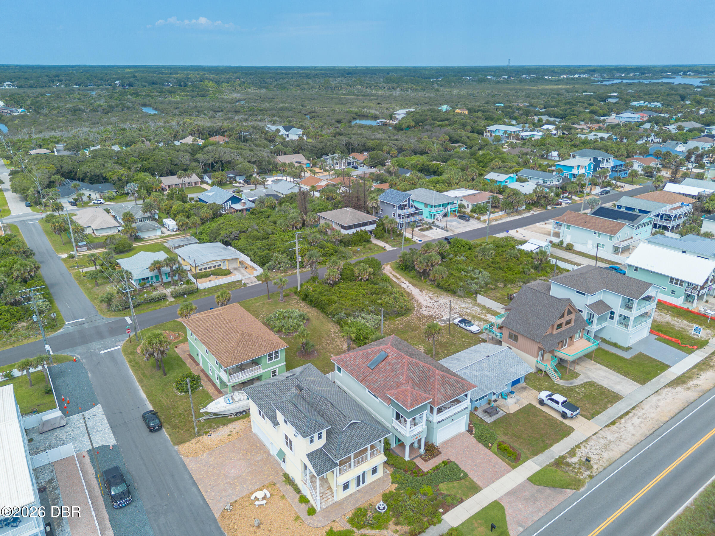 Aerial view of coastal homes beside green wetlands and intersecting streets.