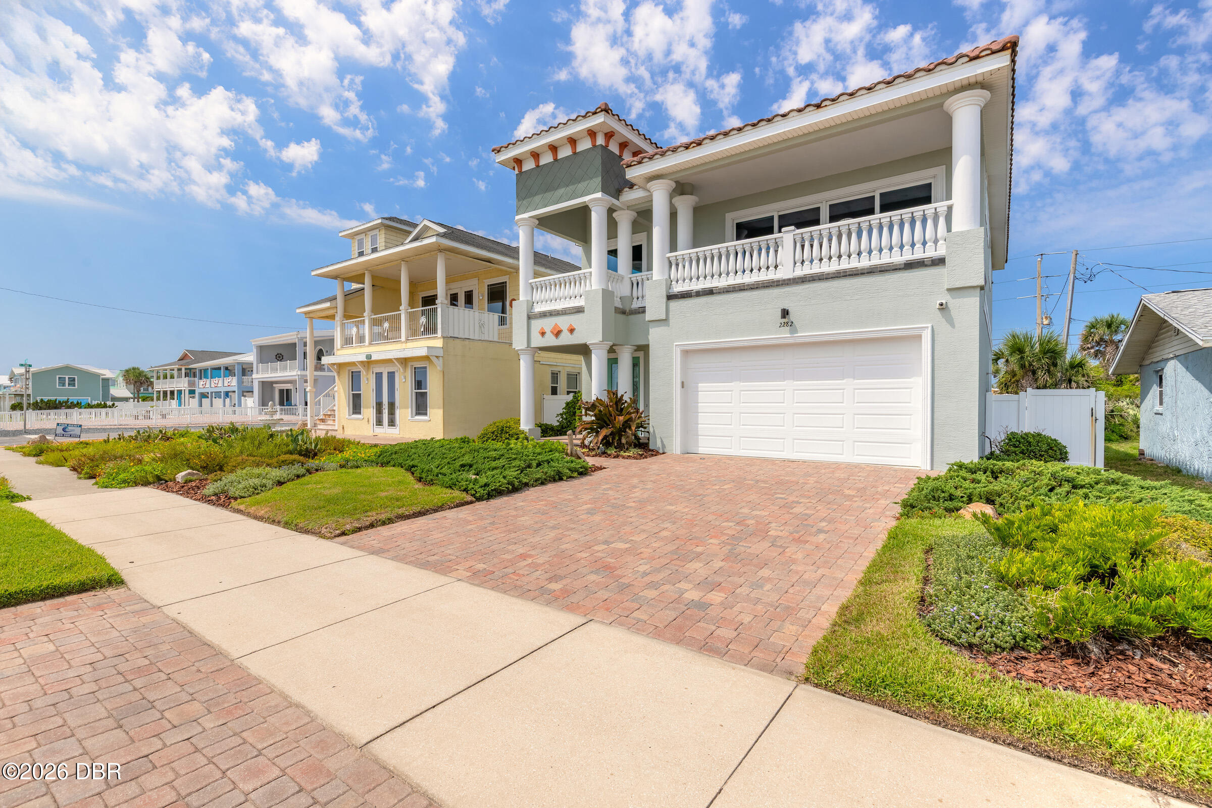 Coastal-style house with white columns, an upper balcony, and a brick driveway.