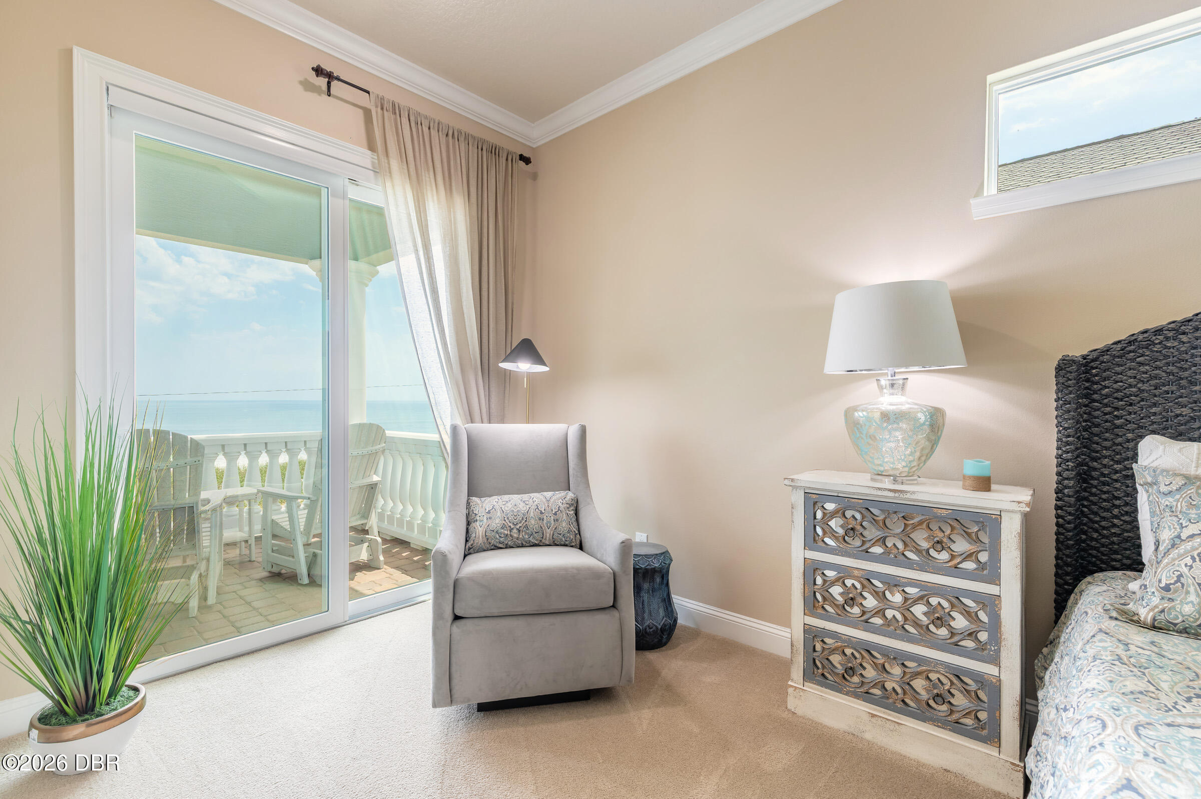 Bedroom sitting area with a gray armchair and sliding glass doors overlooking the ocean.