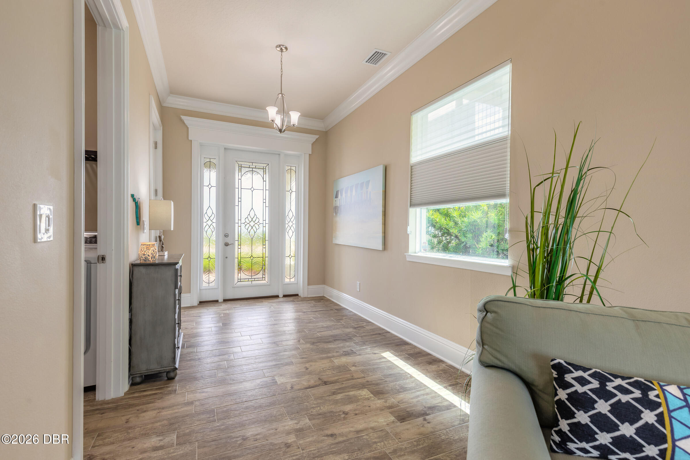 Entry hall with decorative glass front door, wood-look tile flooring, and a chandelier.