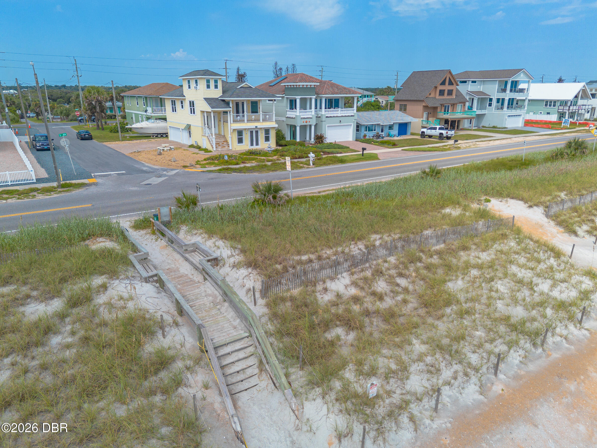 Coastal homes beyond a dune, with a wooden beach access walkway in the foreground.