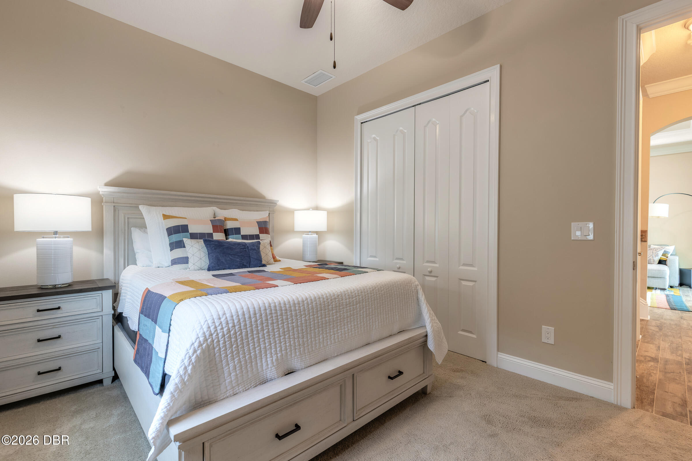 Furnished bedroom with a white bed, colorful patchwork quilt, bedside lamps, and double-door closet.