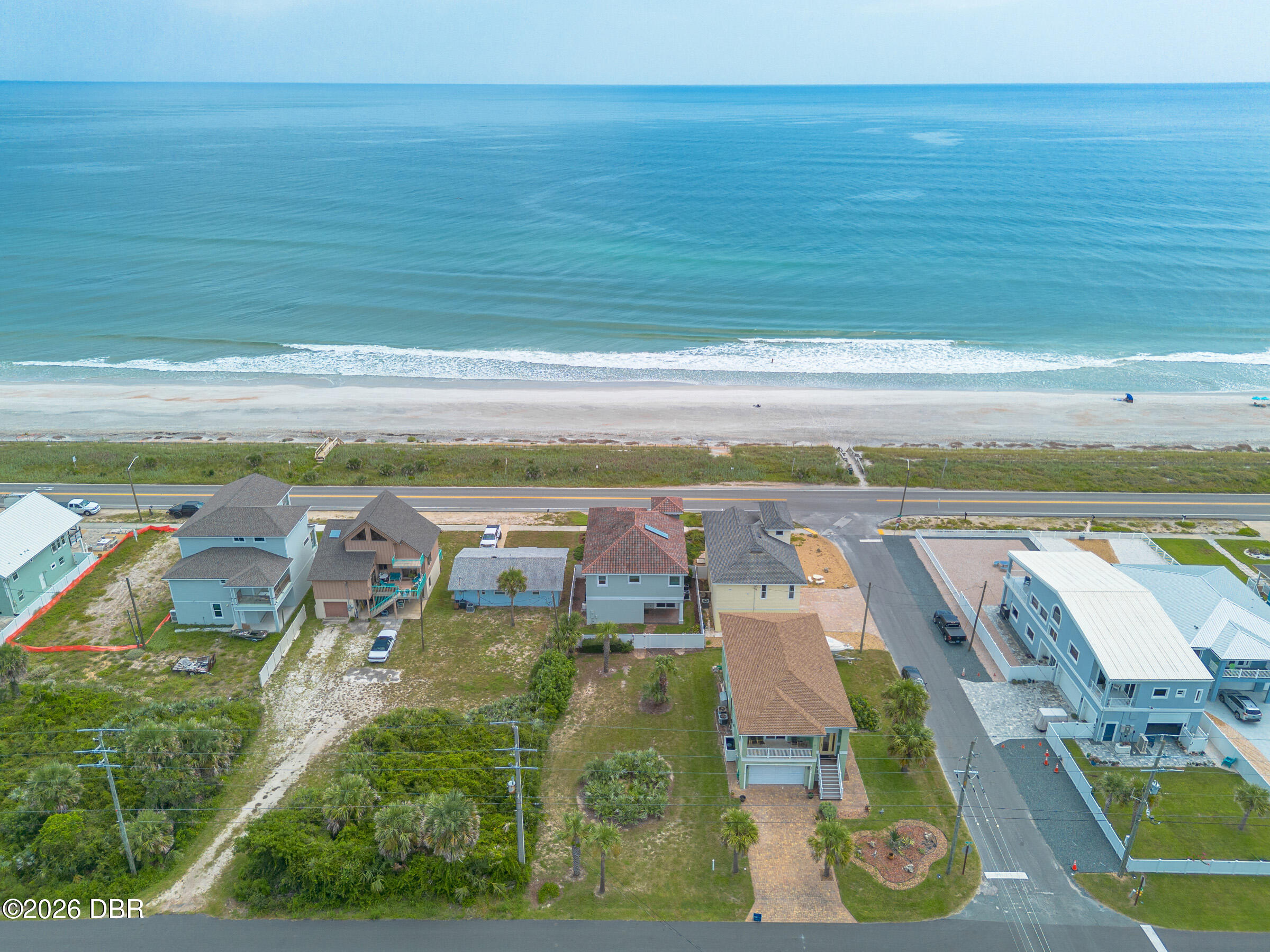 Aerial view of coastal homes beside the beach and ocean, with a road separating them.