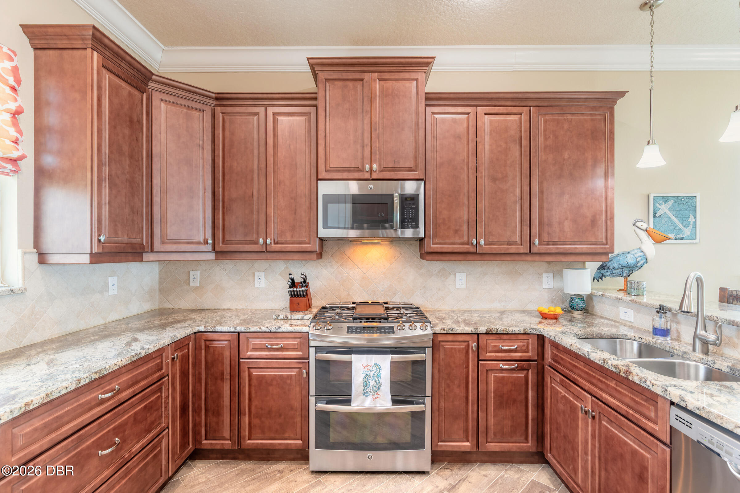 Kitchen with reddish-brown cabinets, stone counters, stainless-steel appliances, and a blue pelican decoration.
