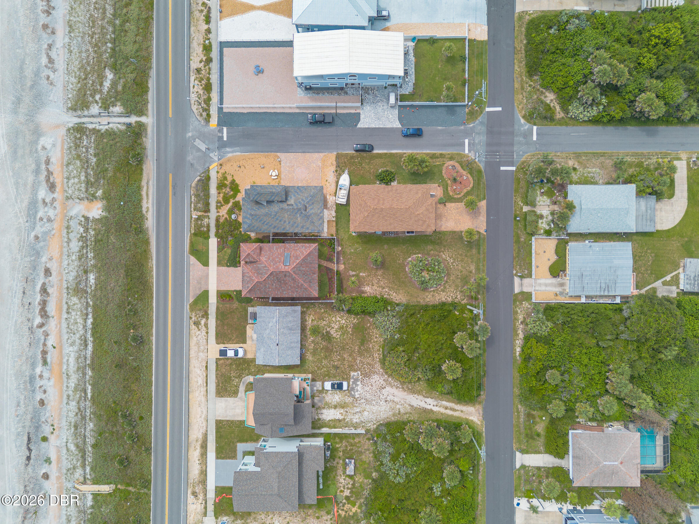 Aerial view of coastal homes beside a sandy shoreline, with a boat parked between two houses.