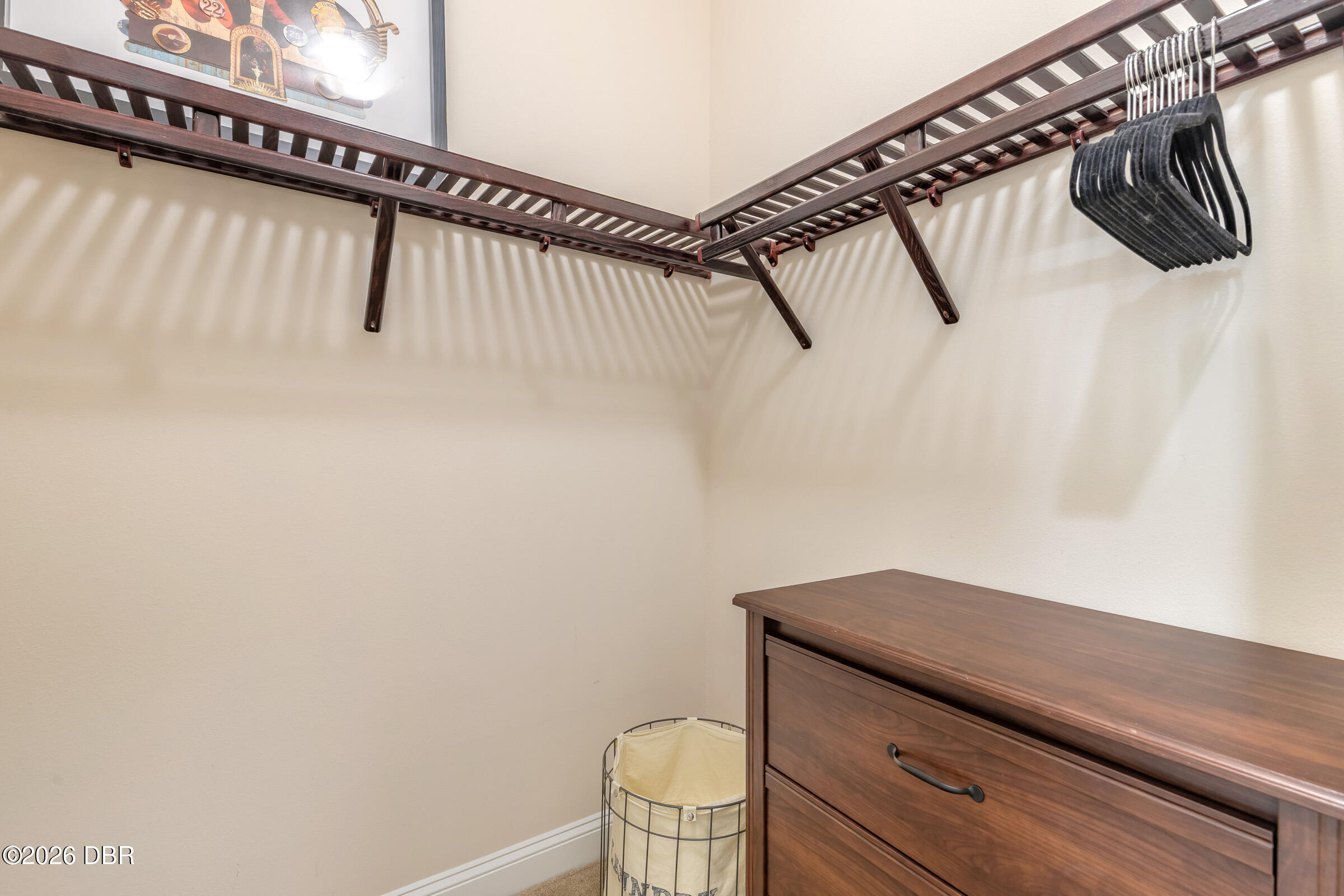 Walk-in closet with wraparound wooden hanging racks, black hangers, and a dark wood dresser.