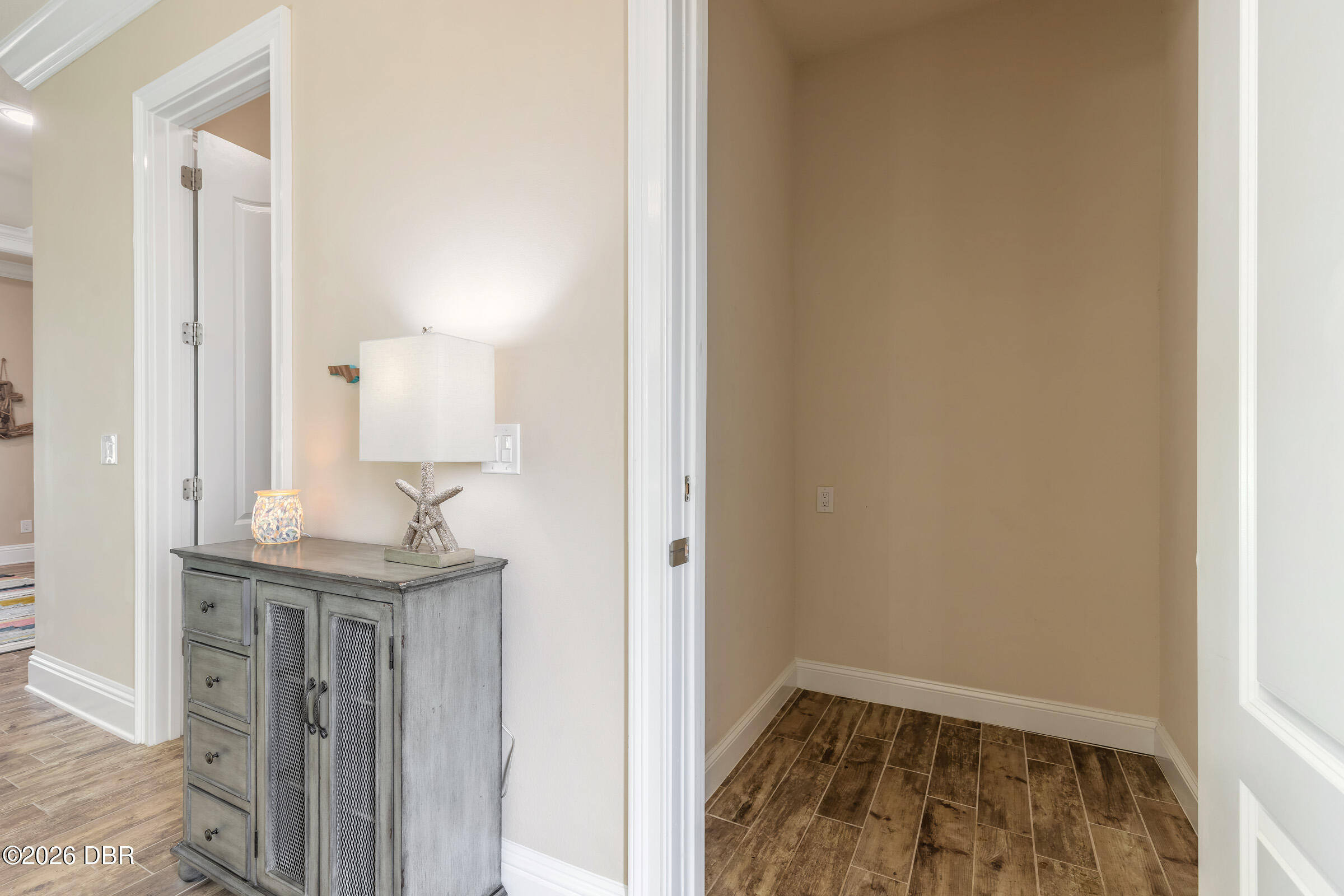 Entry hall with a gray console cabinet and lamp beside an empty alcove with wood-look tile flooring.