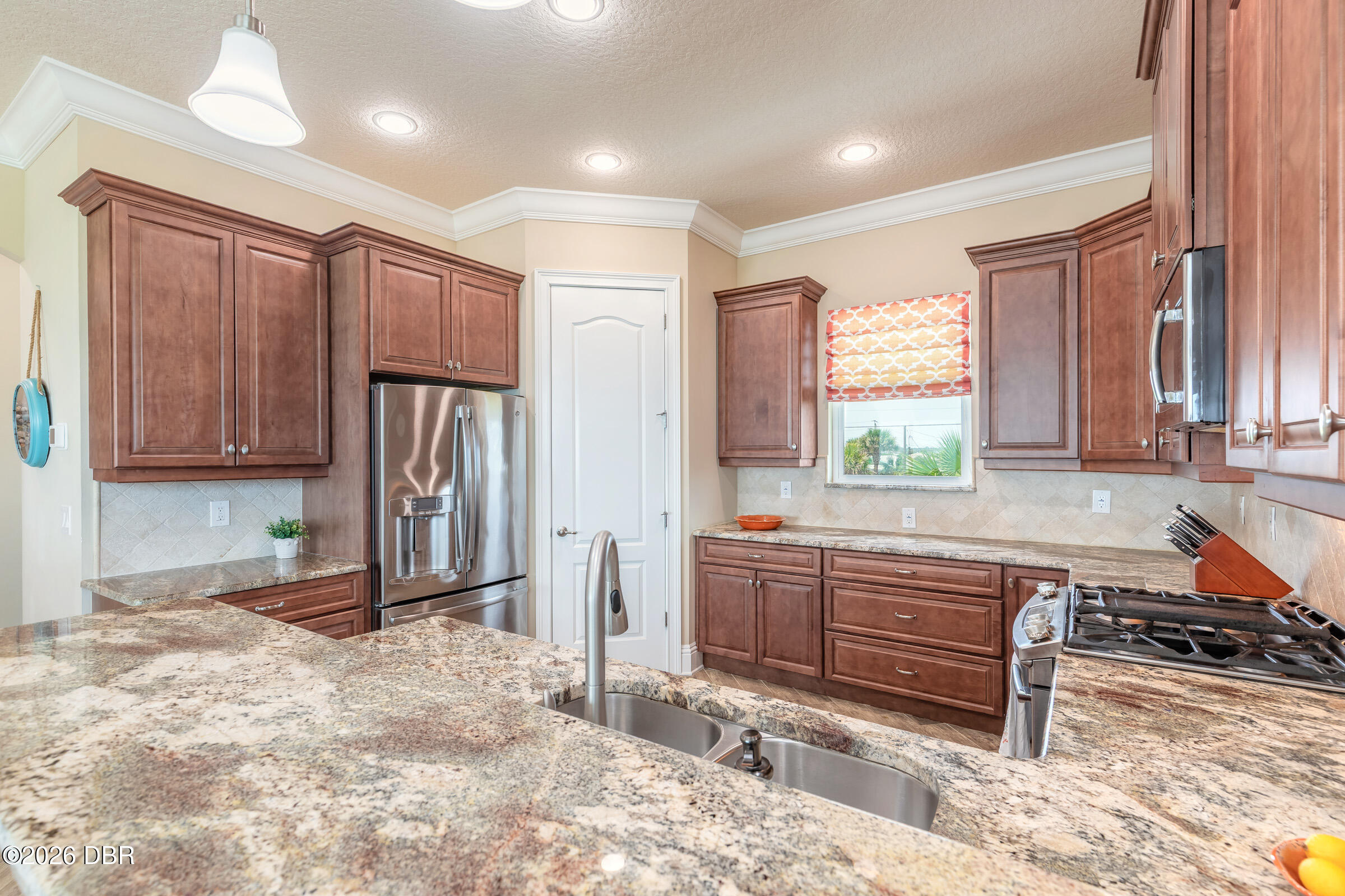 Kitchen with reddish-brown cabinets, granite counters, stainless appliances, and a large island sink.