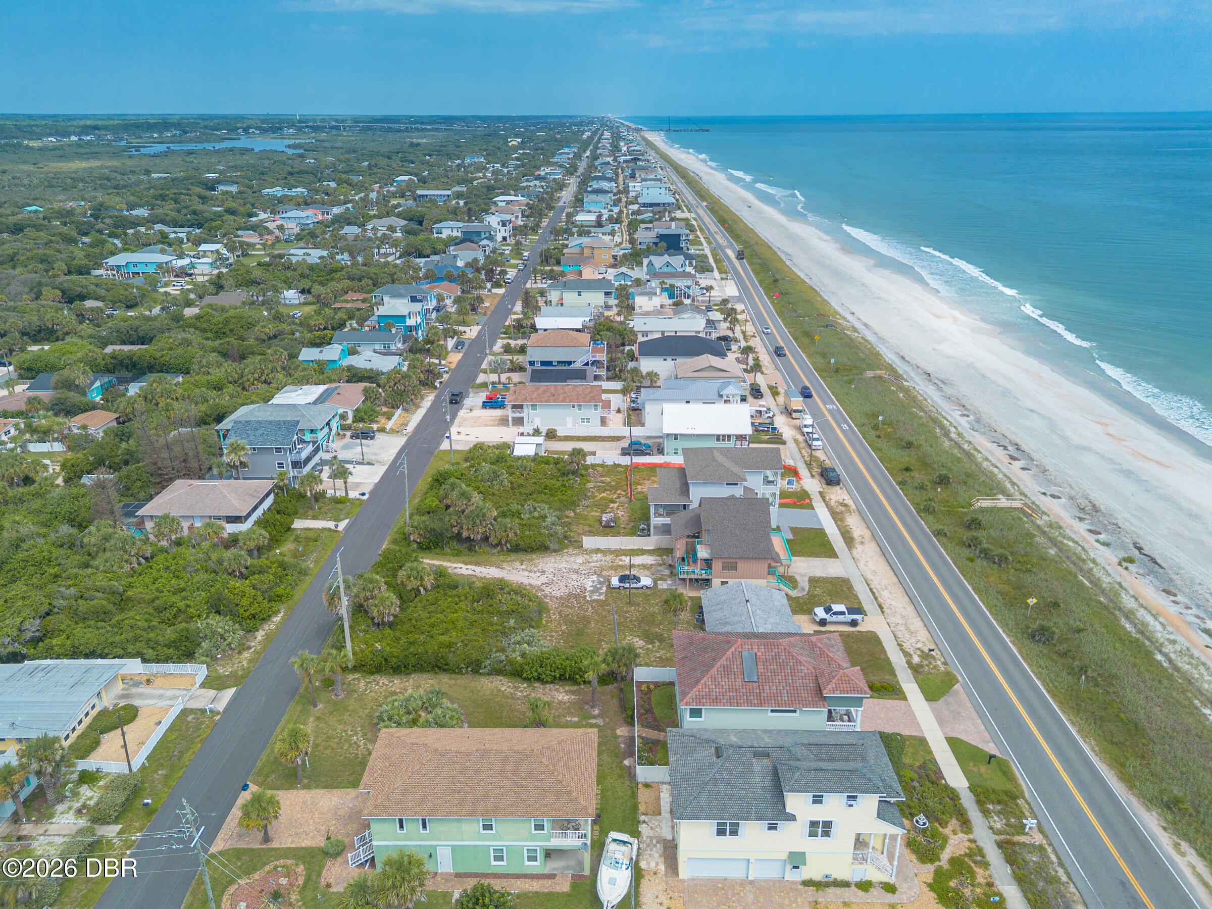 Aerial view of coastal homes beside the beach, ocean, and parallel shoreline road.