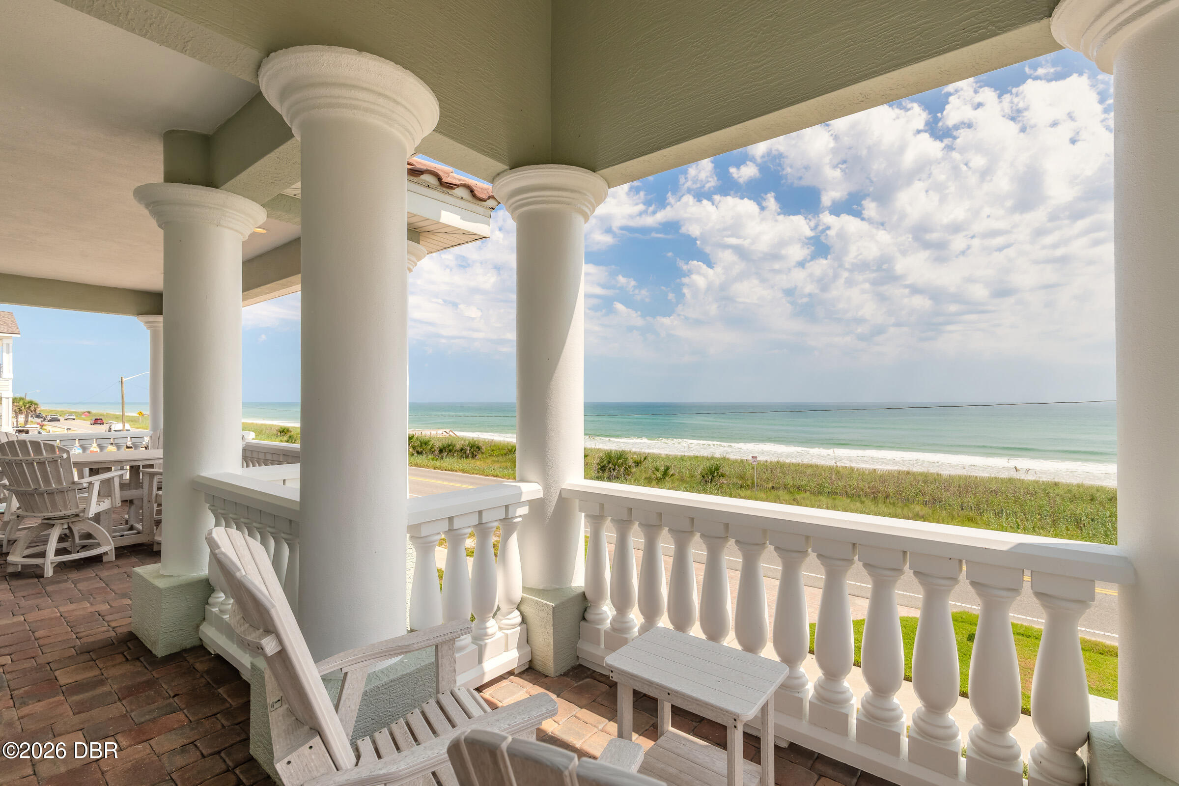 Covered porch with white columns and Adirondack chairs overlooking dunes, beach, and ocean.