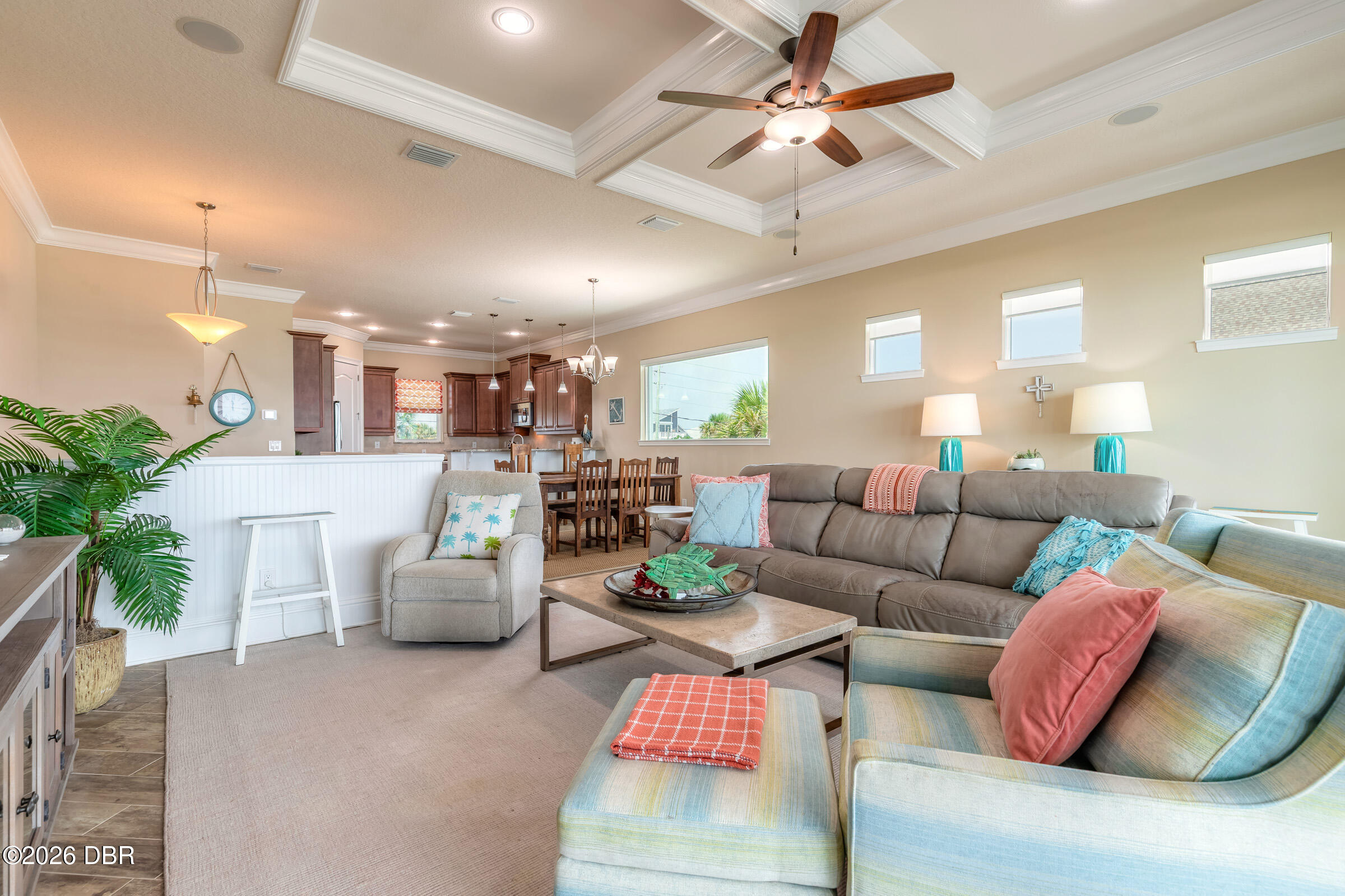 Open-plan living room with a gray sectional, pale blue armchairs, and a coffered ceiling.
