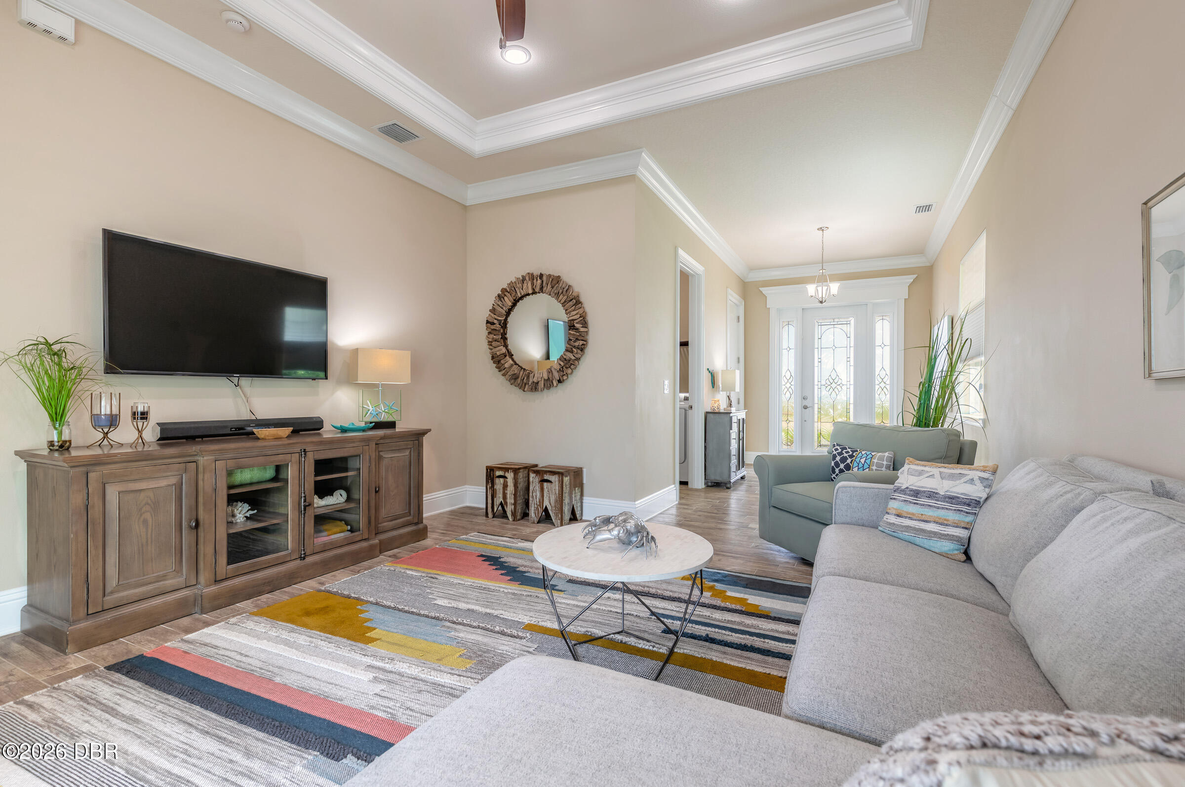 Living room with gray sectional, sage-green loveseat, colorful rug, and bright glass-paneled doors.