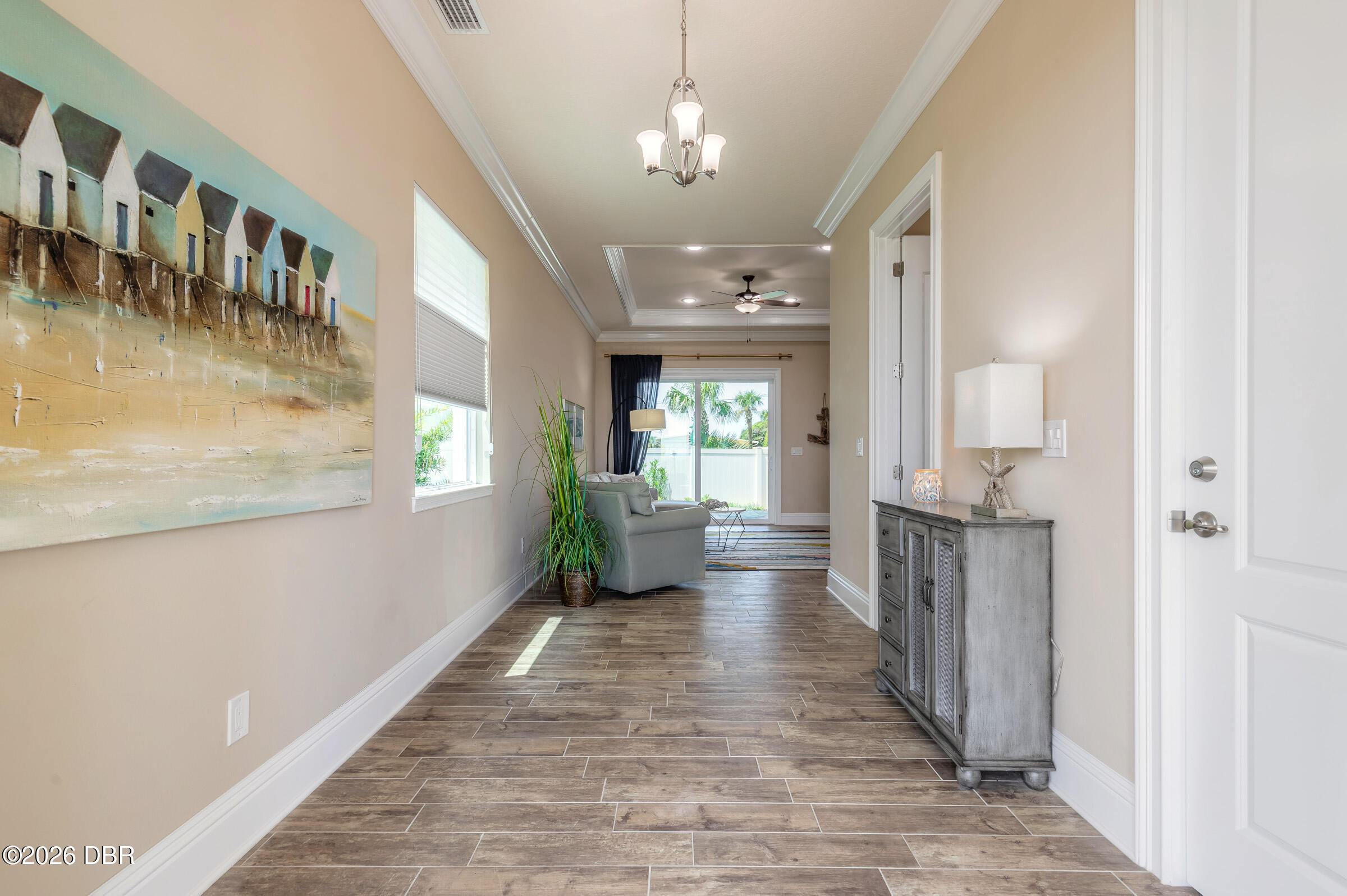 Furnished entry hallway with wood-look tile, beach-hut artwork, and a view into the living area.