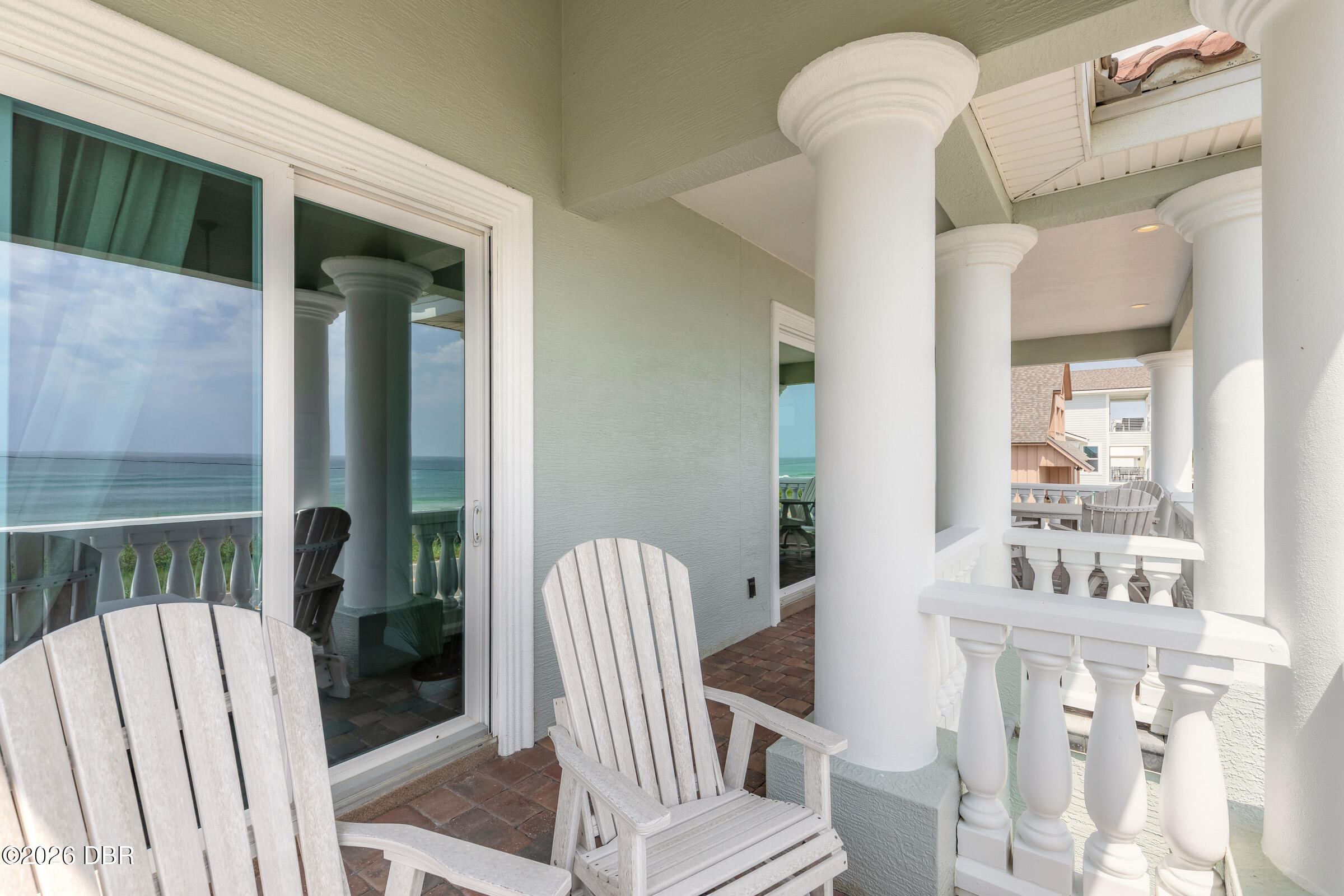 Covered porch with white columns and Adirondack chairs overlooking the ocean.