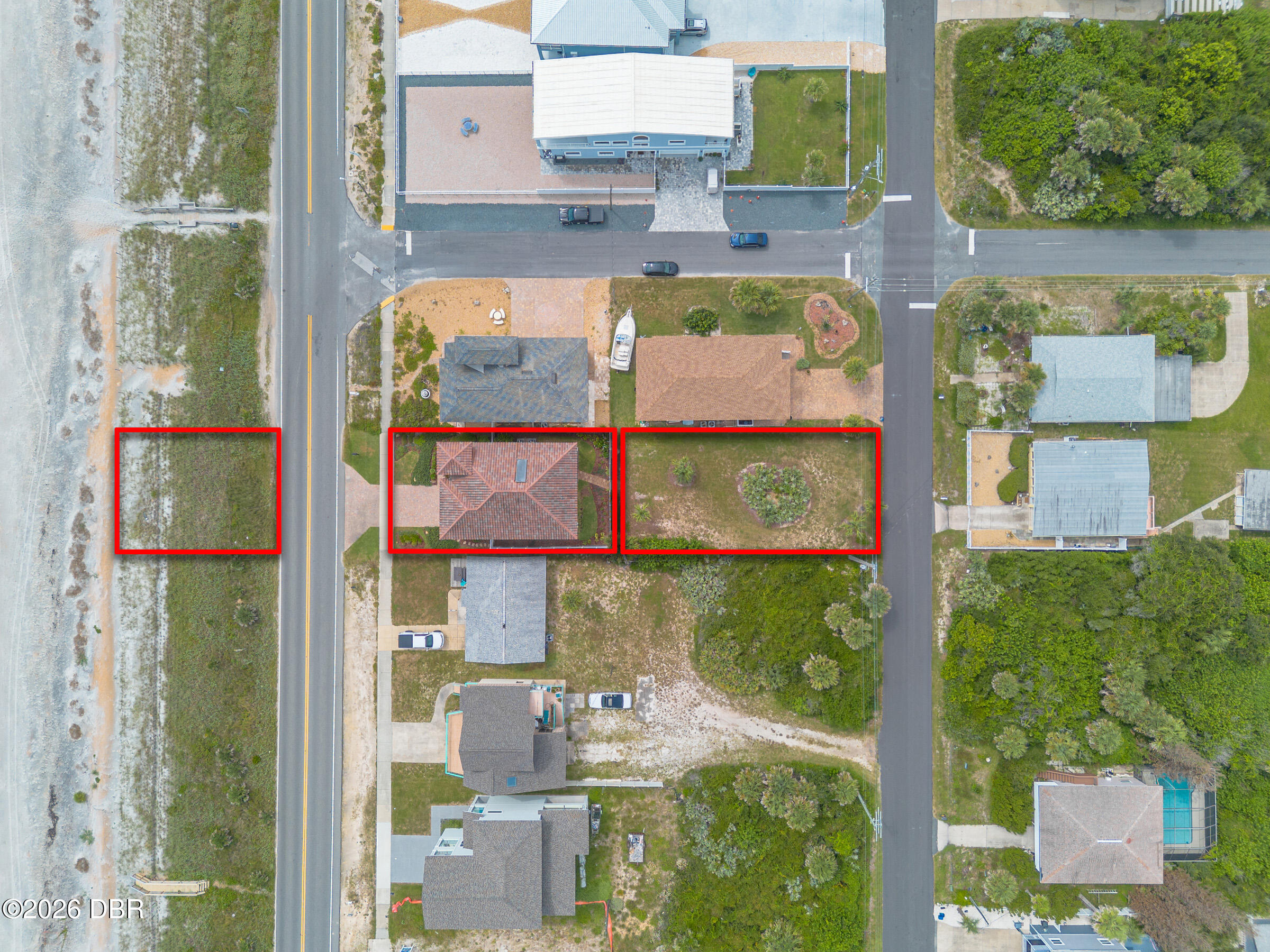 Aerial view of a red-outlined home and adjacent parcels beside the beach and coastal road.