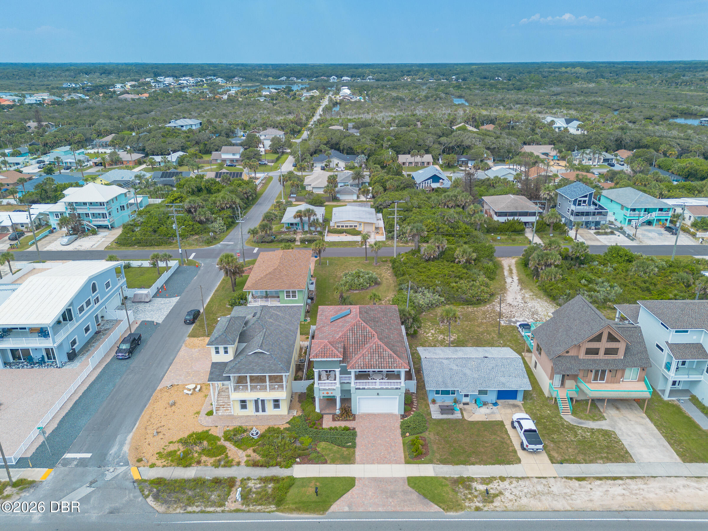 Aerial view of a red-tile-roof home among coastal neighborhood houses and greenery.