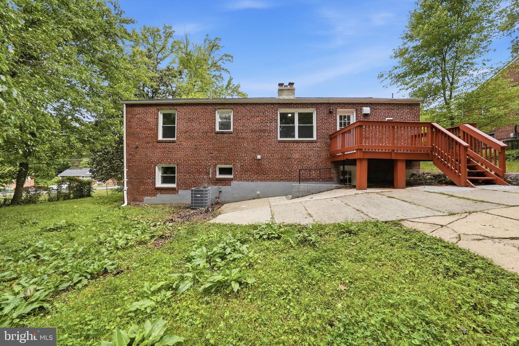 Rear of a red-brick house with a raised wooden deck and concrete driveway.