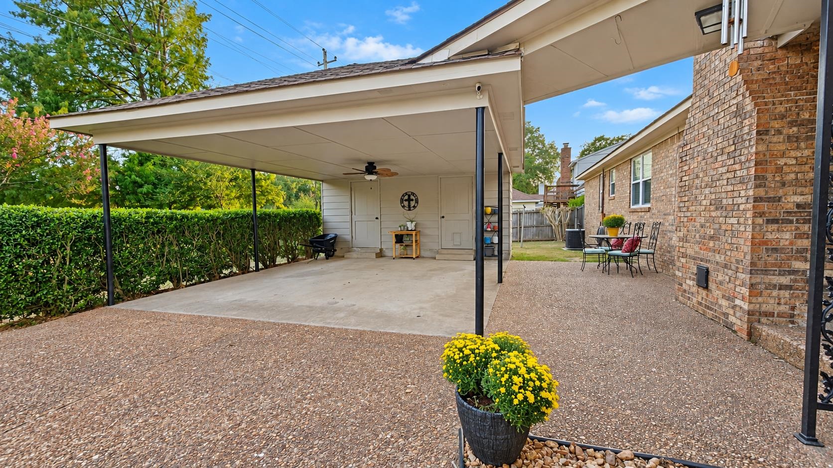Covered patio beside a brick house, with a ceiling fan and outdoor seating.