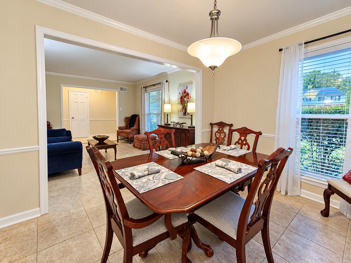 Furnished dining room with a carved wooden table beside a large curtained window.