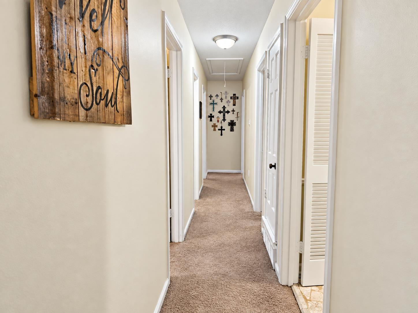 Carpeted hallway with white doors and a collection of crosses displayed on the far wall.