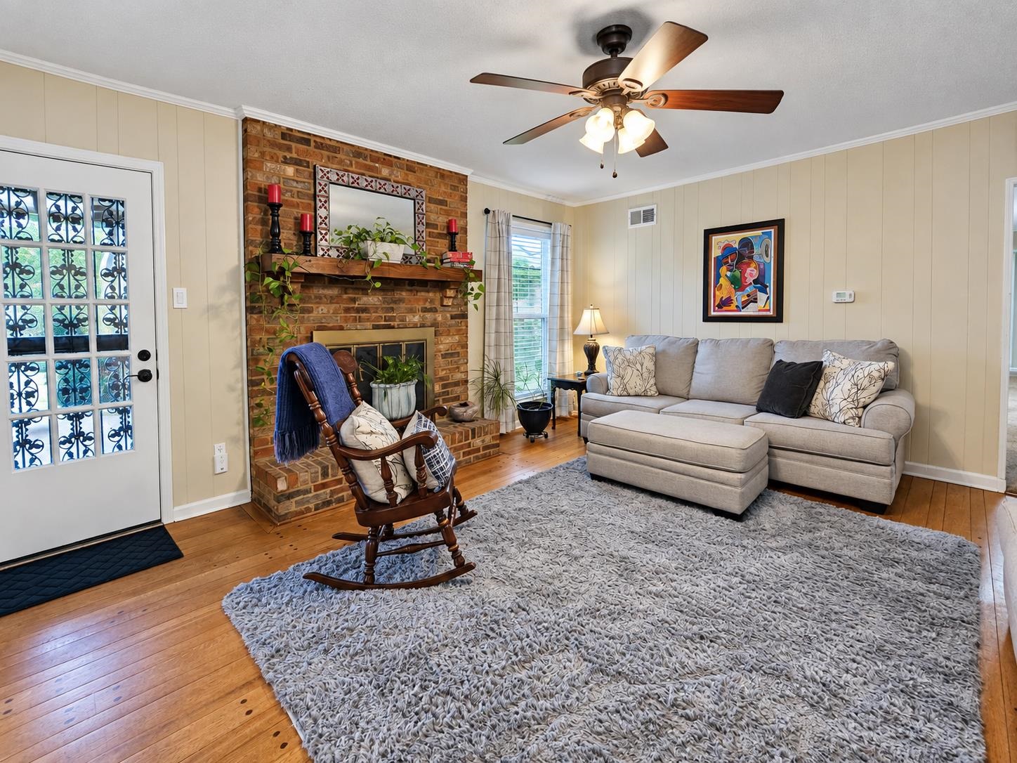 Living room with brick fireplace, gray sectional, rocking chair, and a large shag rug.