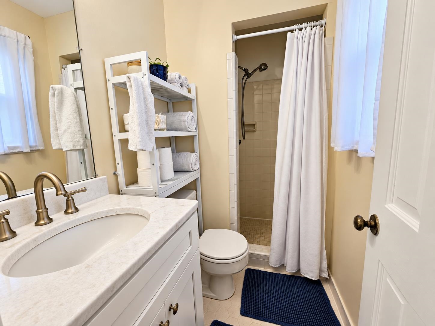 Bathroom with a marble-look vanity, tiled shower, and open shelving stocked with towels.