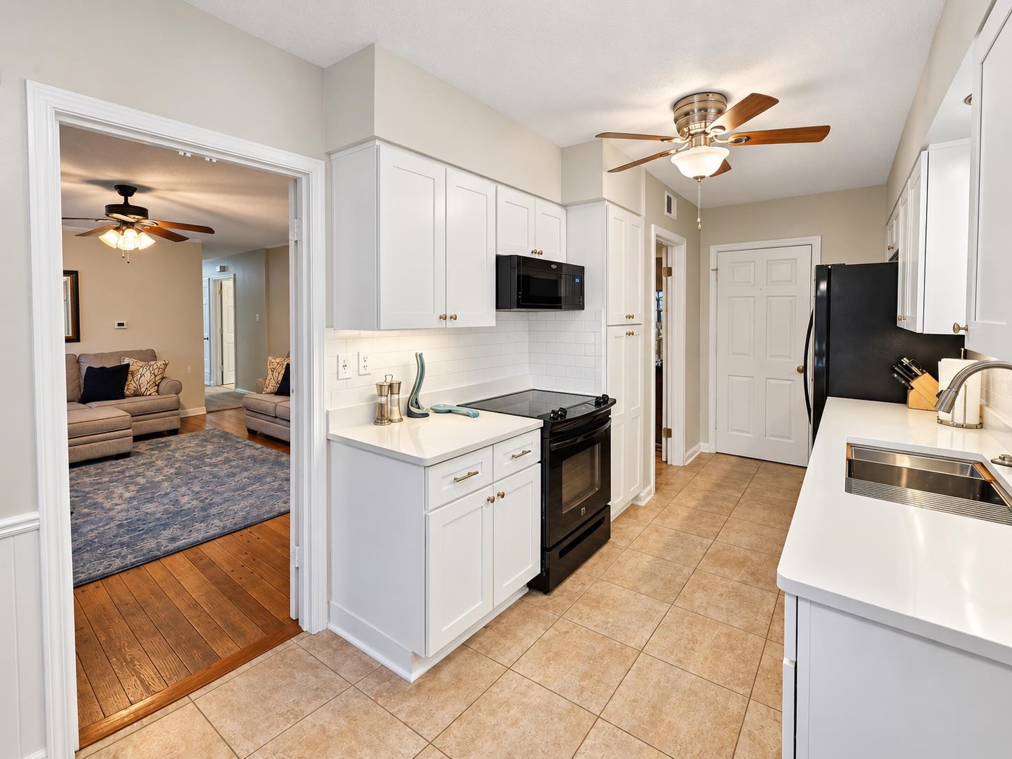 Kitchen with white cabinets and black appliances, opening onto a living room with hardwood floors.