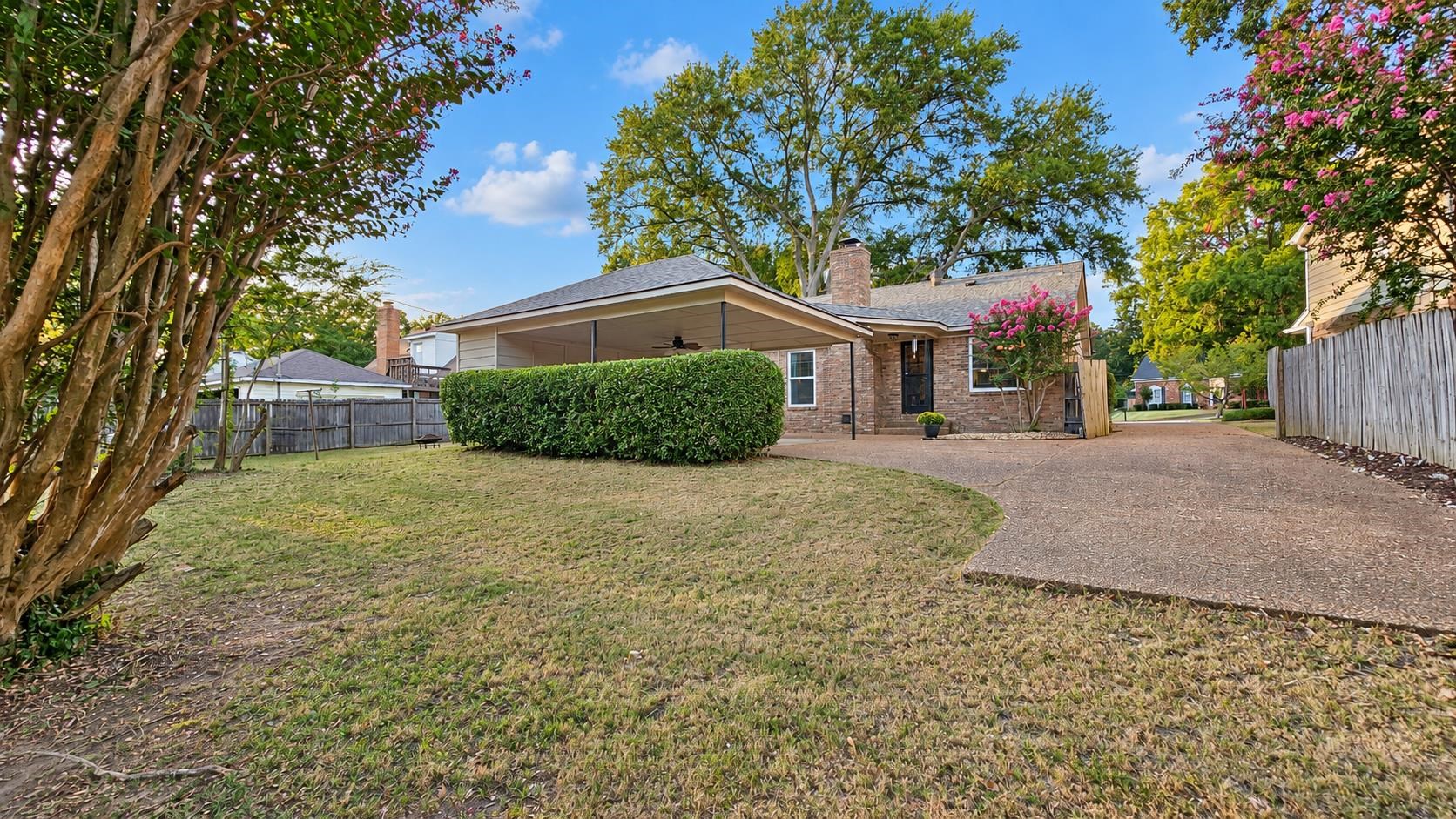 Brick home's rear exterior with a covered patio, paved driveway, and fenced yard.