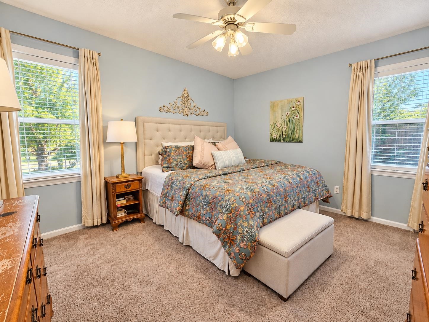 Bedroom with a blue floral comforter, upholstered headboard, and windows on two walls.