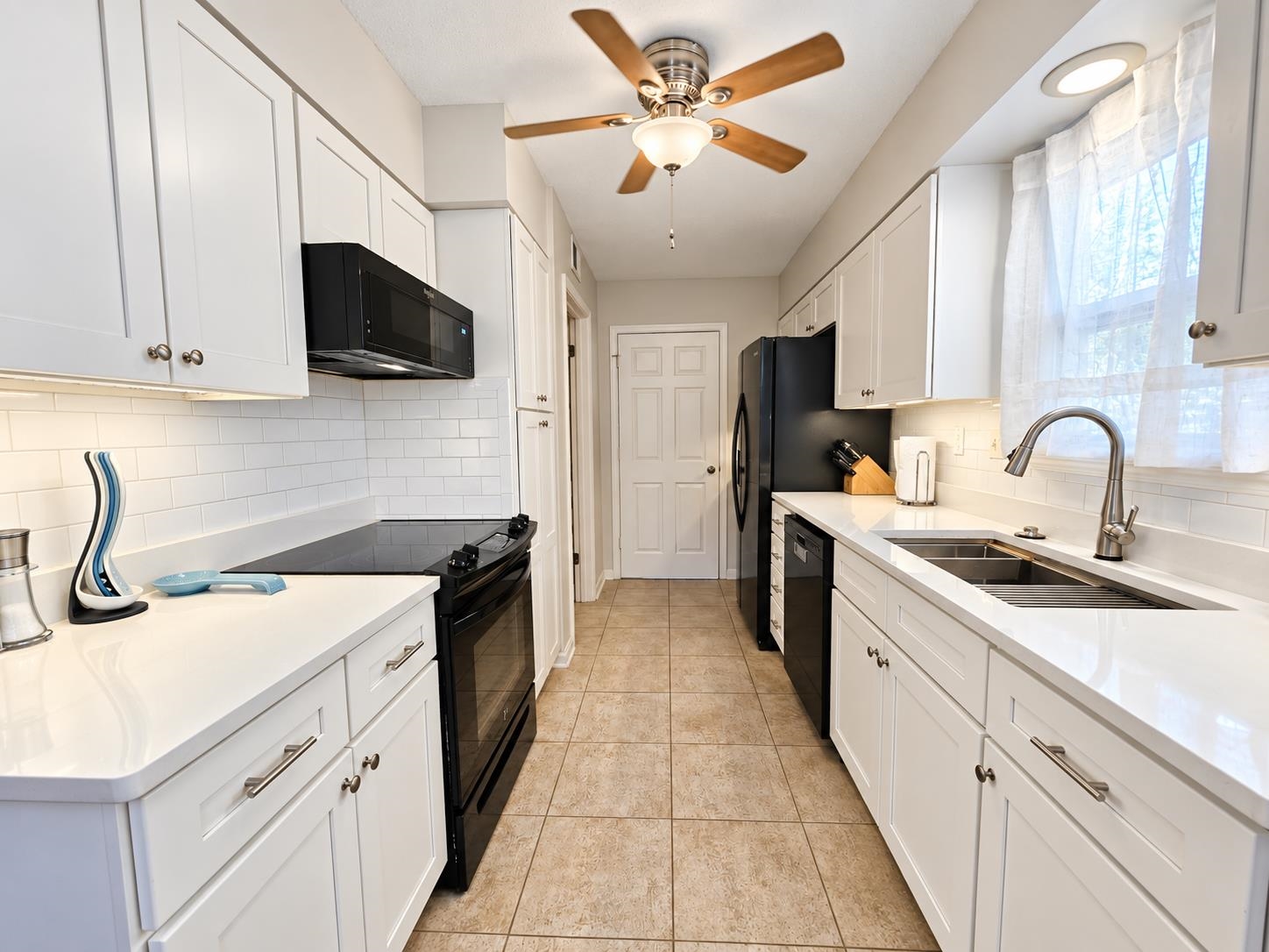 Kitchen with white cabinets and counters, black appliances, and a double-basin sink beneath a window.