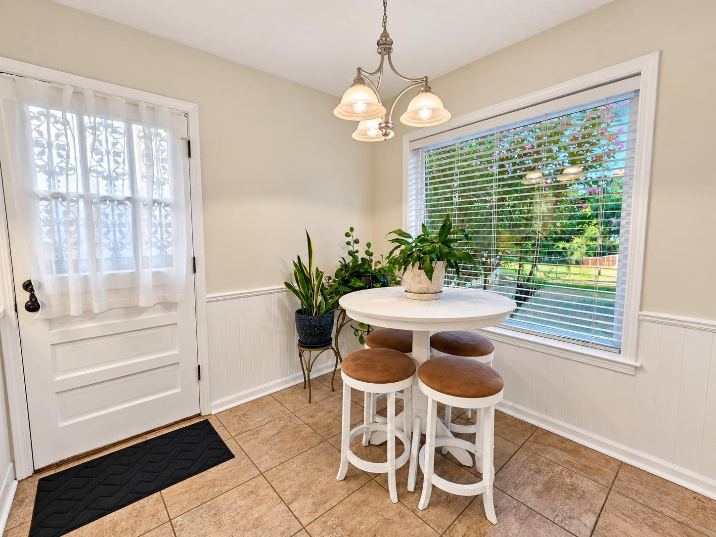 Breakfast nook with a round table, brown-cushioned stools, potted plants, and a window overlooking the yard.