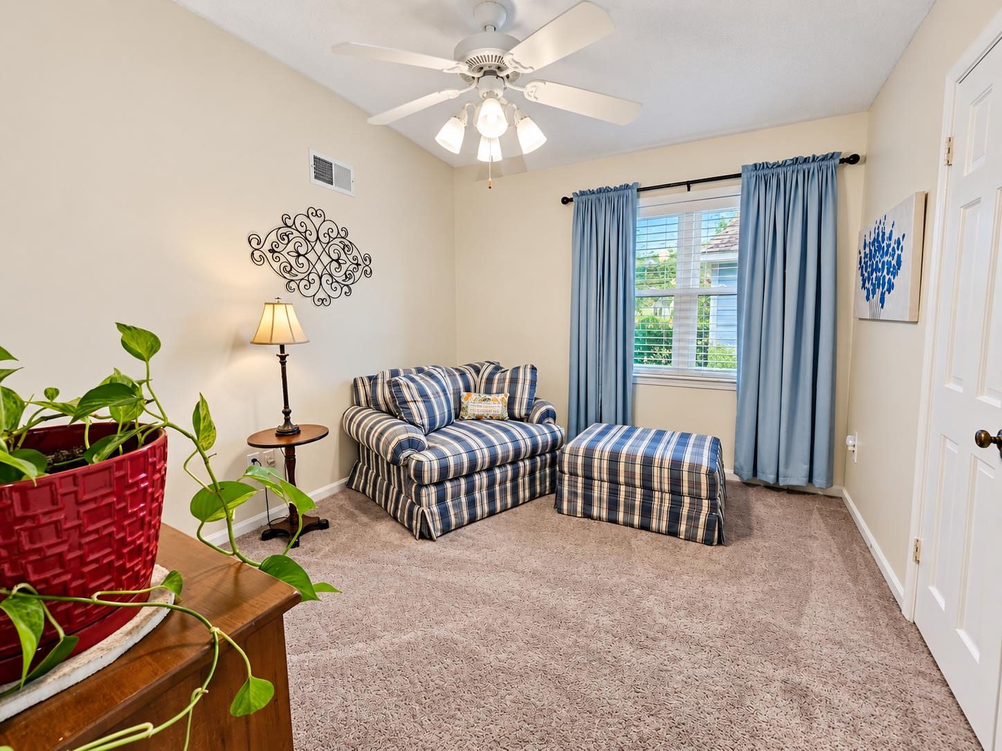 Sitting room with a plaid loveseat and ottoman, blue curtains, and a ceiling fan.