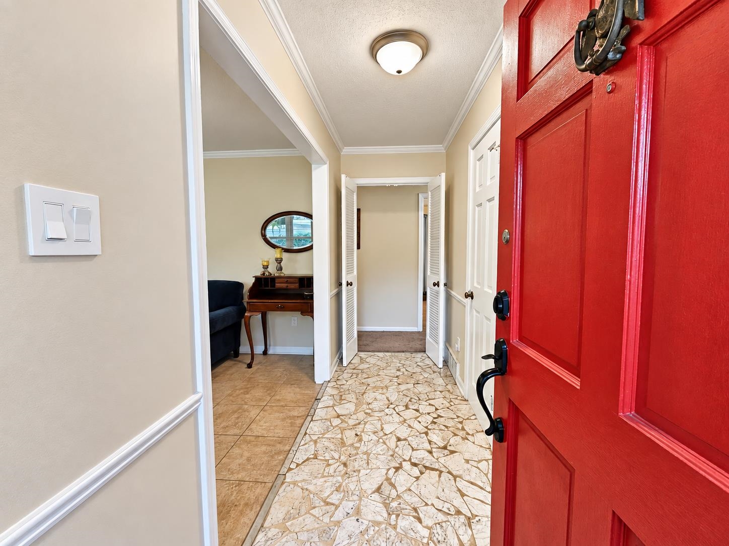 Entry hall with a bright red front door, patterned tile floor, and a small furnished sitting area.