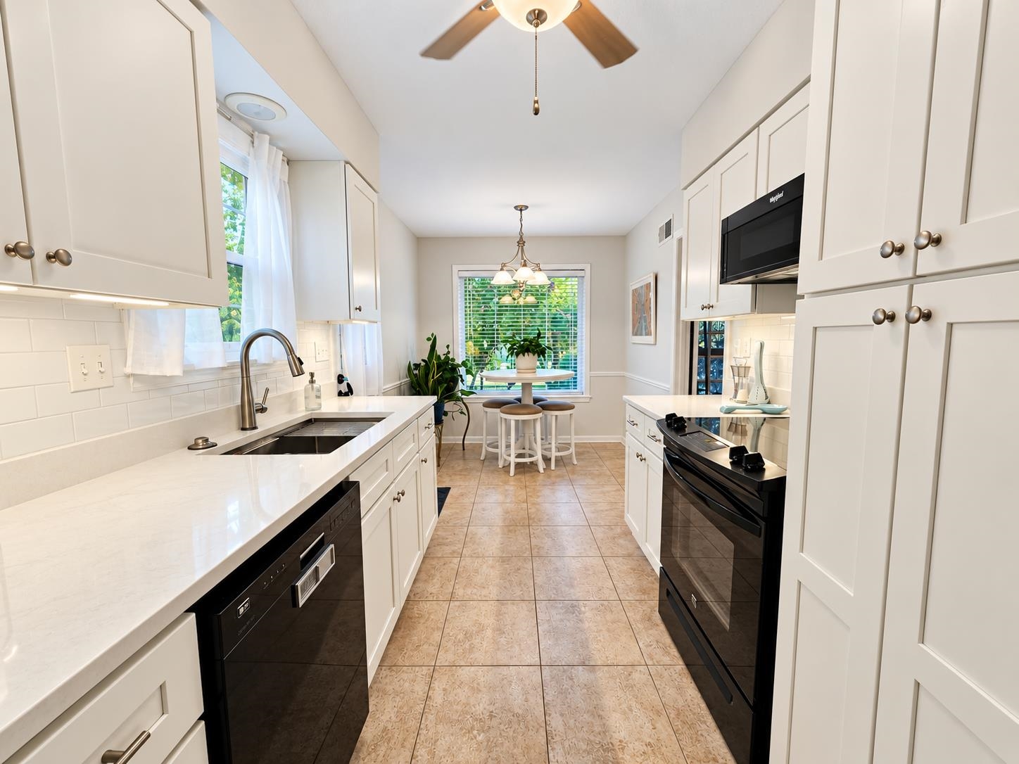 Bright white galley kitchen with black appliances and a small dining table by the window.