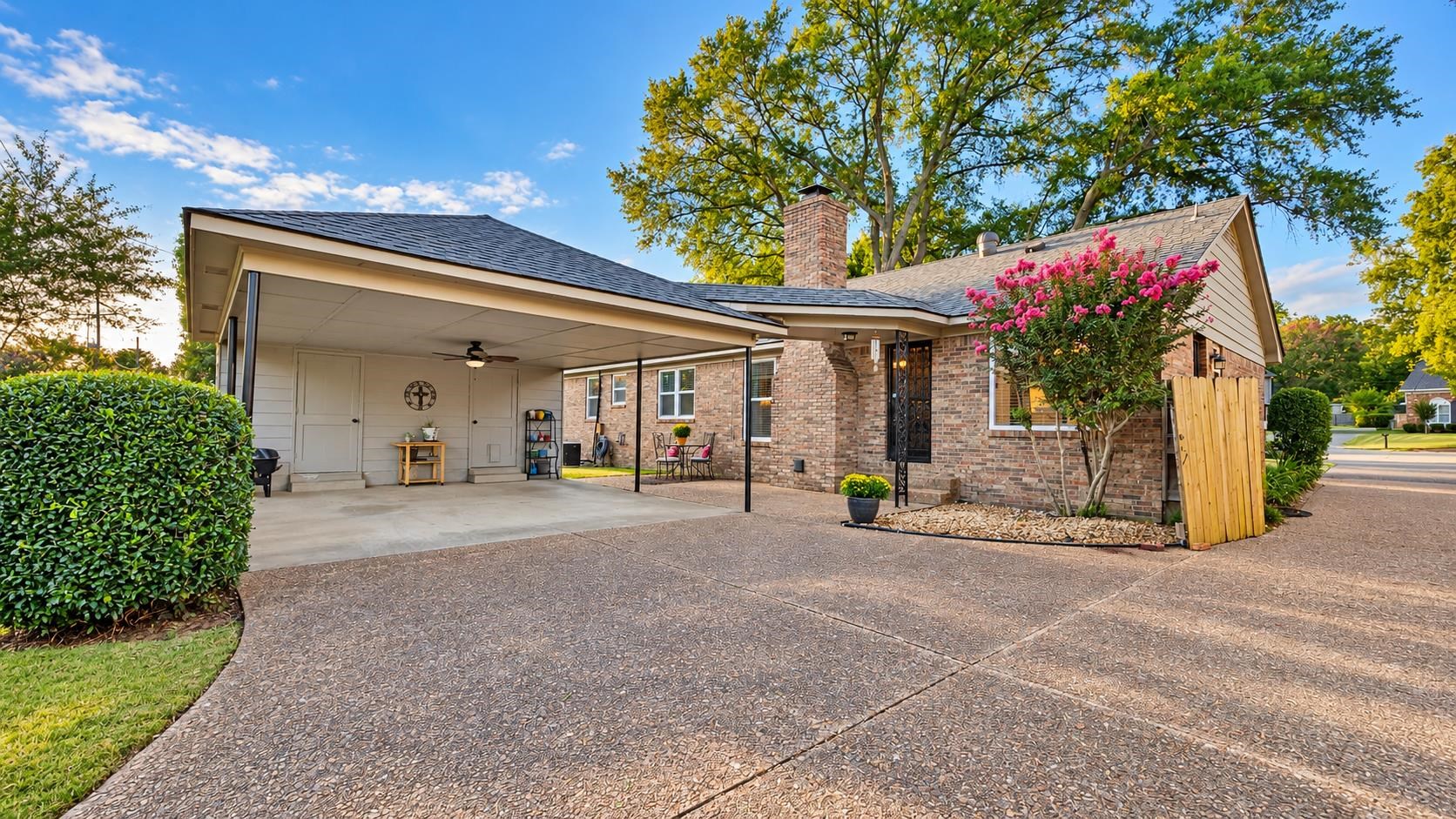 Brick home with a covered carport and wide patterned driveway, framed by a pink flowering tree.