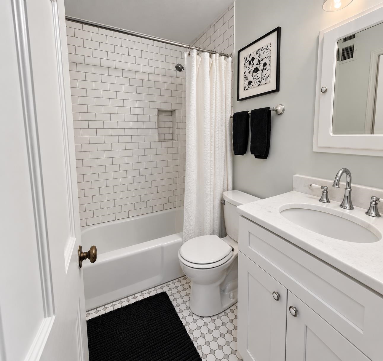 Bathroom with a white subway-tile tub and shower, white vanity, and geometric tile floor.