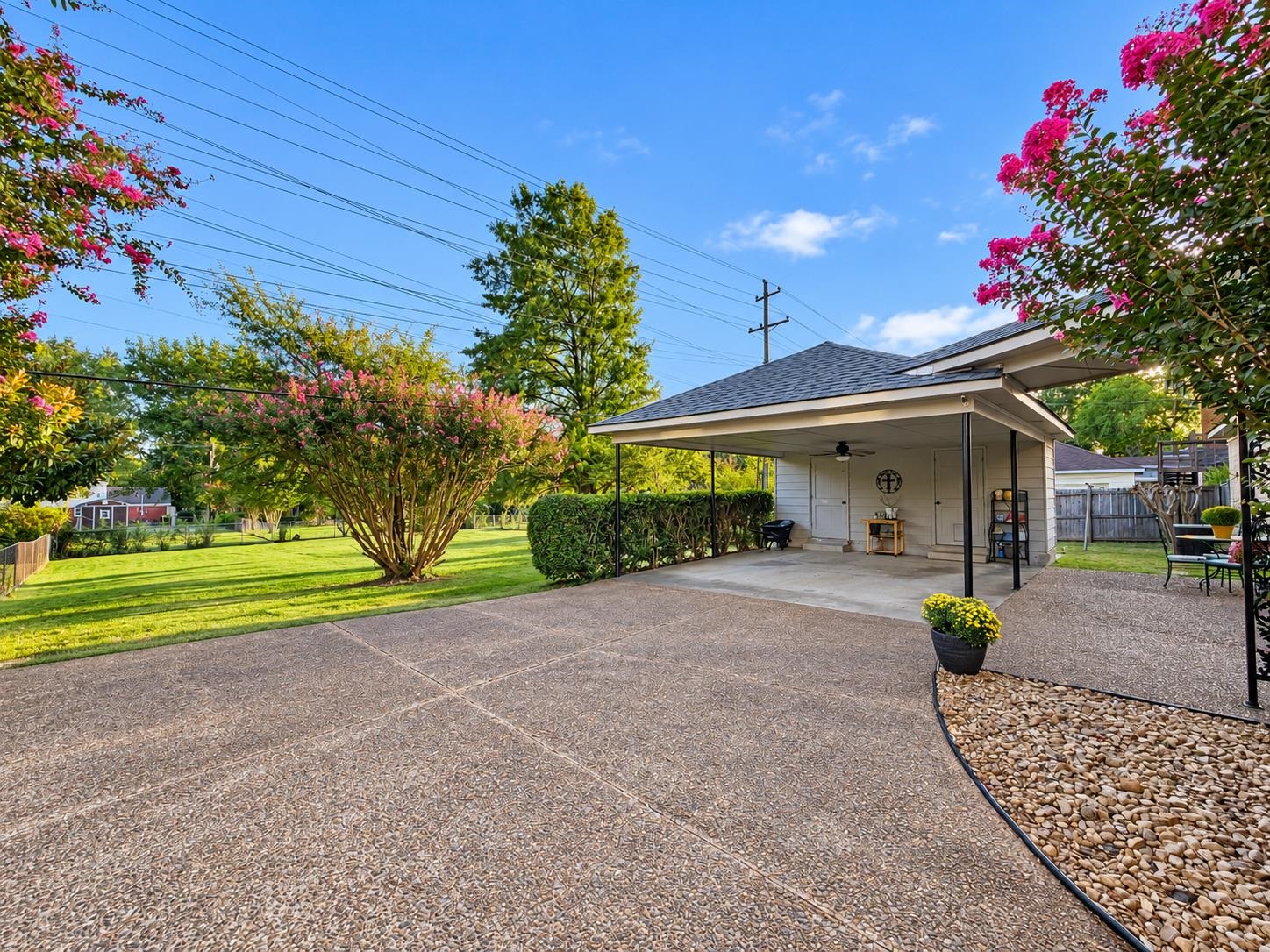 Backyard patio with a covered pavilion, outdoor furniture, flowering trees, and a broad lawn.