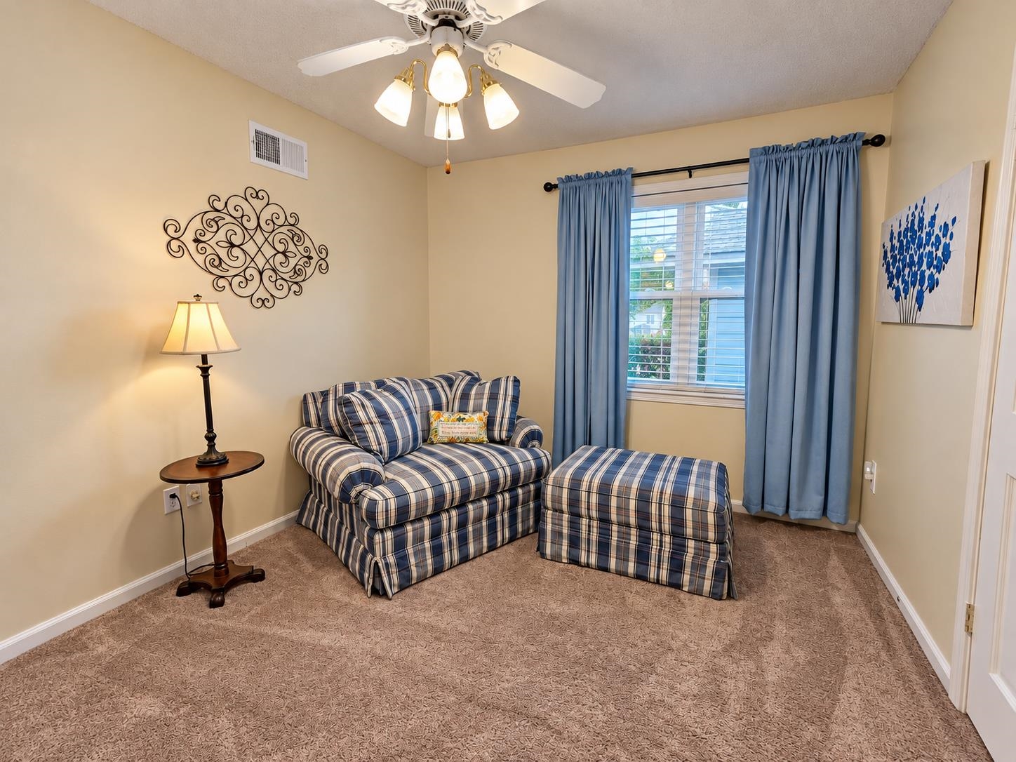 Furnished sitting room with a blue plaid loveseat and matching ottoman beside a curtained window.