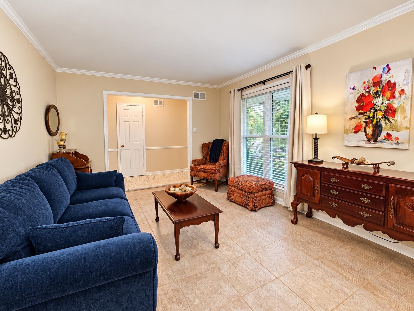 Furnished living room with a blue sofa, wooden furniture, patterned armchair, and large curtained window.