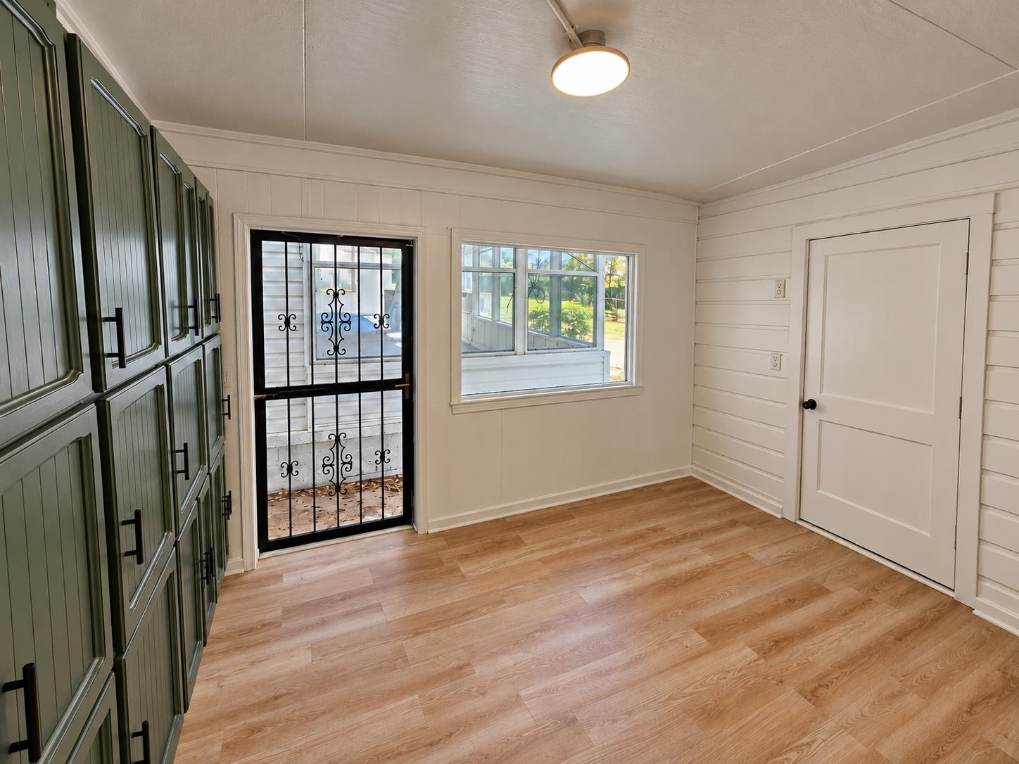 Empty room with green built-in cabinets, wood flooring, a window, and a decorative security door.