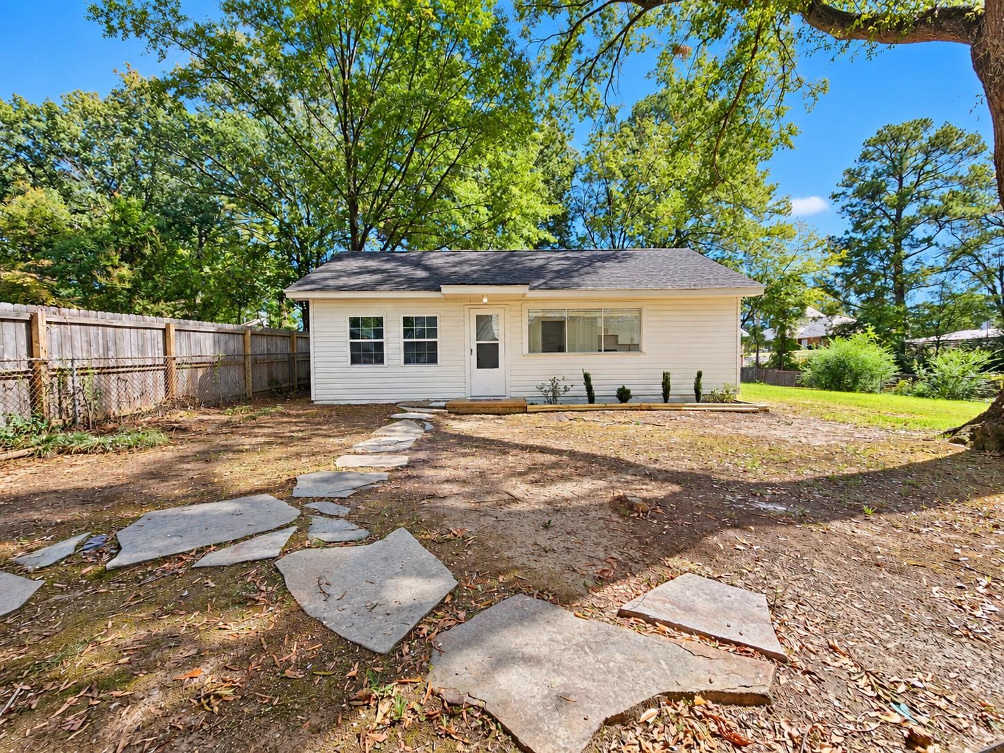 Rear of a white single-story house beyond a stepping-stone path in a tree-shaded backyard.