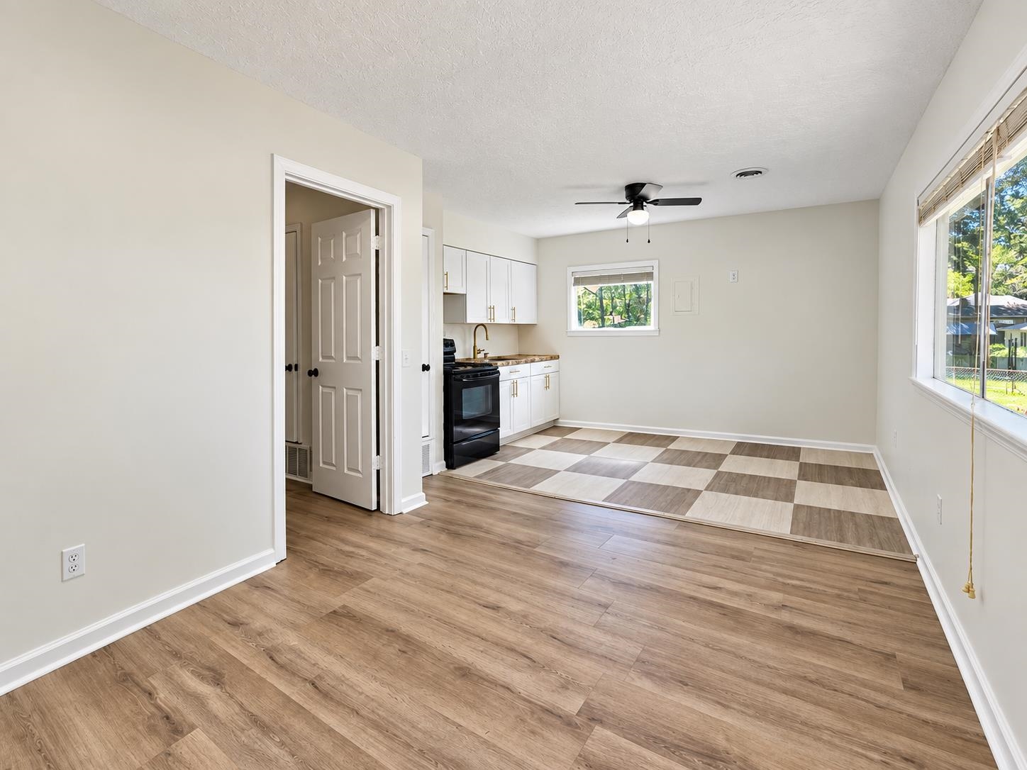 Vacant kitchen and dining area with white cabinets, black stove, and checkerboard tile flooring.