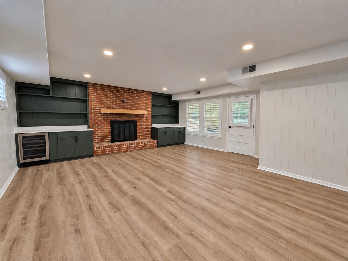 Unfurnished living room with a brick fireplace, dark built-ins, and light wood-look flooring.