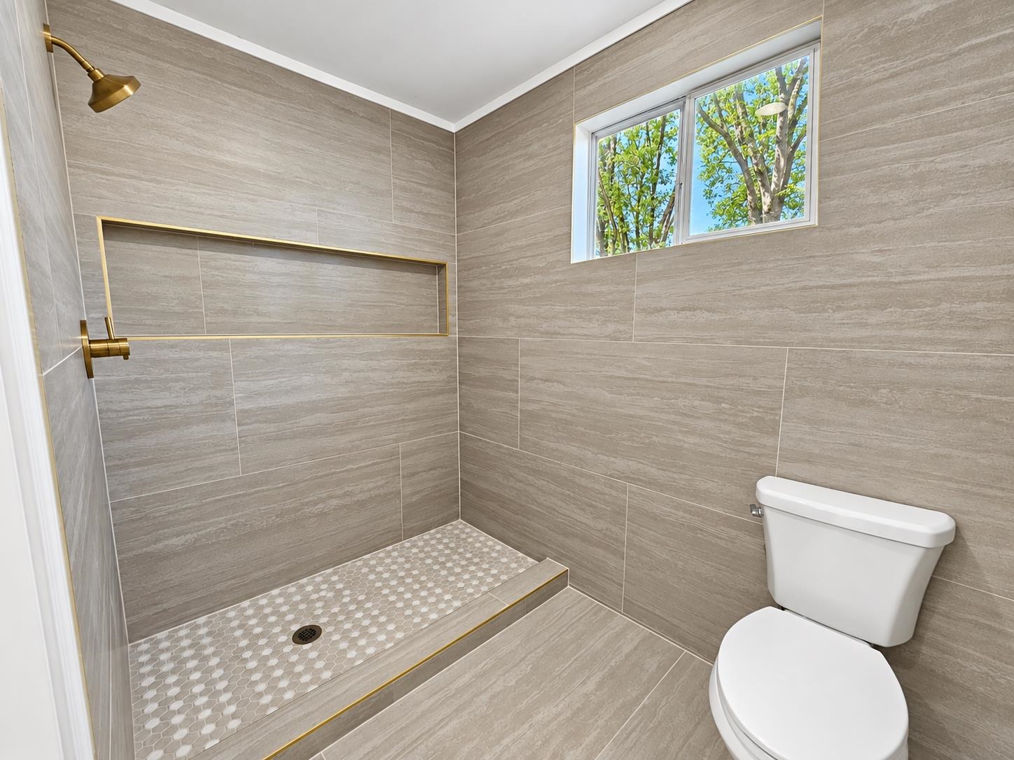 Bathroom with a tiled walk-in shower, gold-tone fixtures, mosaic floor, and high window.
