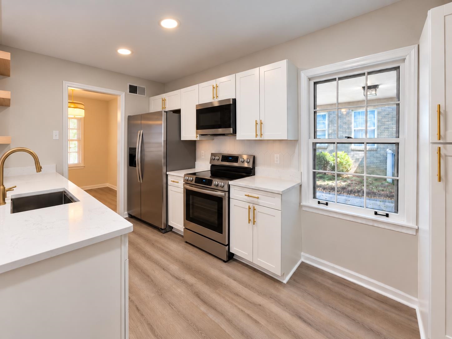 Renovated kitchen with white cabinets, stainless steel appliances, gold hardware, and a large island.