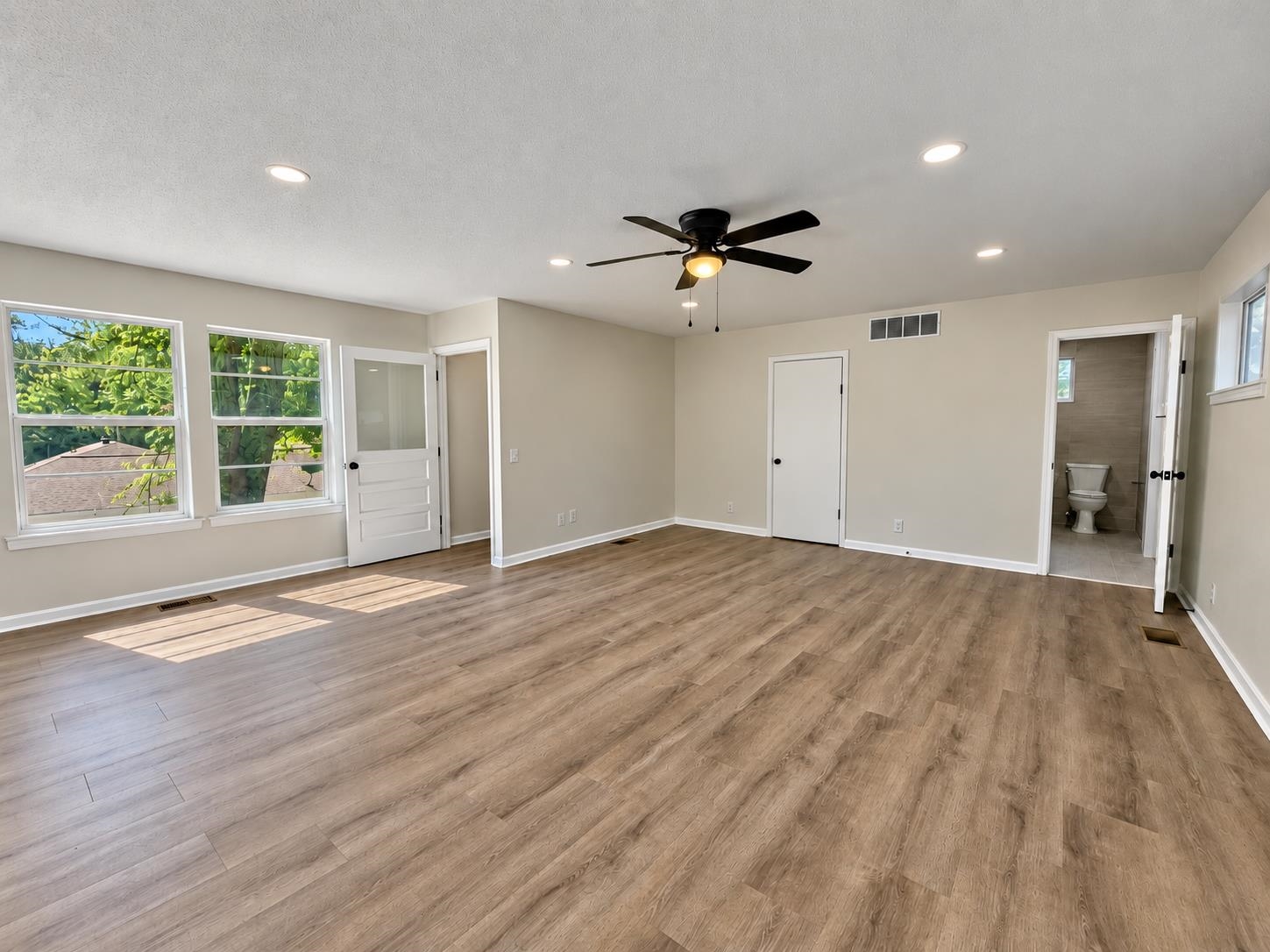 Empty bedroom with wood-look flooring, a ceiling fan, and an adjoining bathroom.
